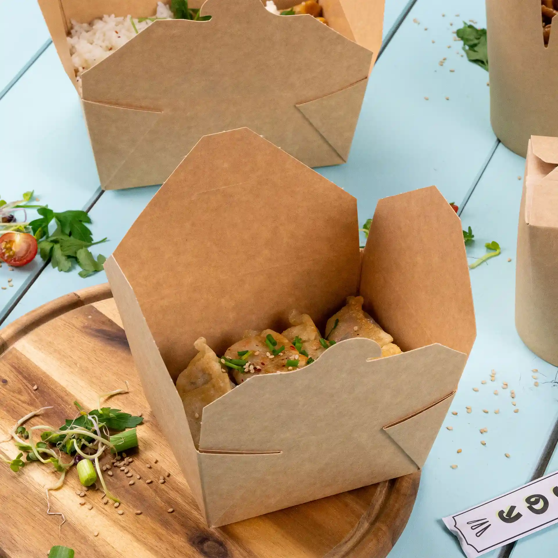 Braune Papp-Take-away-Box mit Teigtaschen, auf einer Holzoberfläche mit verstreuten Zutaten.
