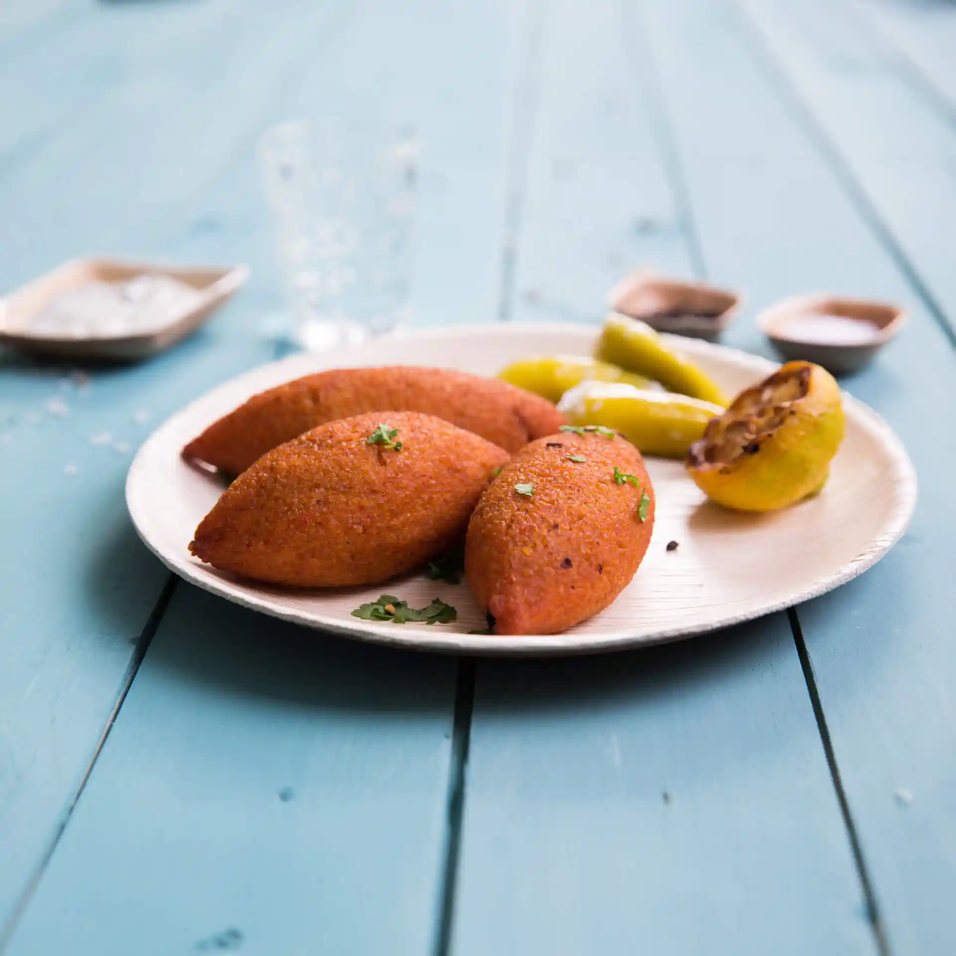 Teller mit drei orangefarbenen Gegenständen, garniert mit Kräutern, dazu gelbe Paprika und eine gegrillte Zitronenscheibe.