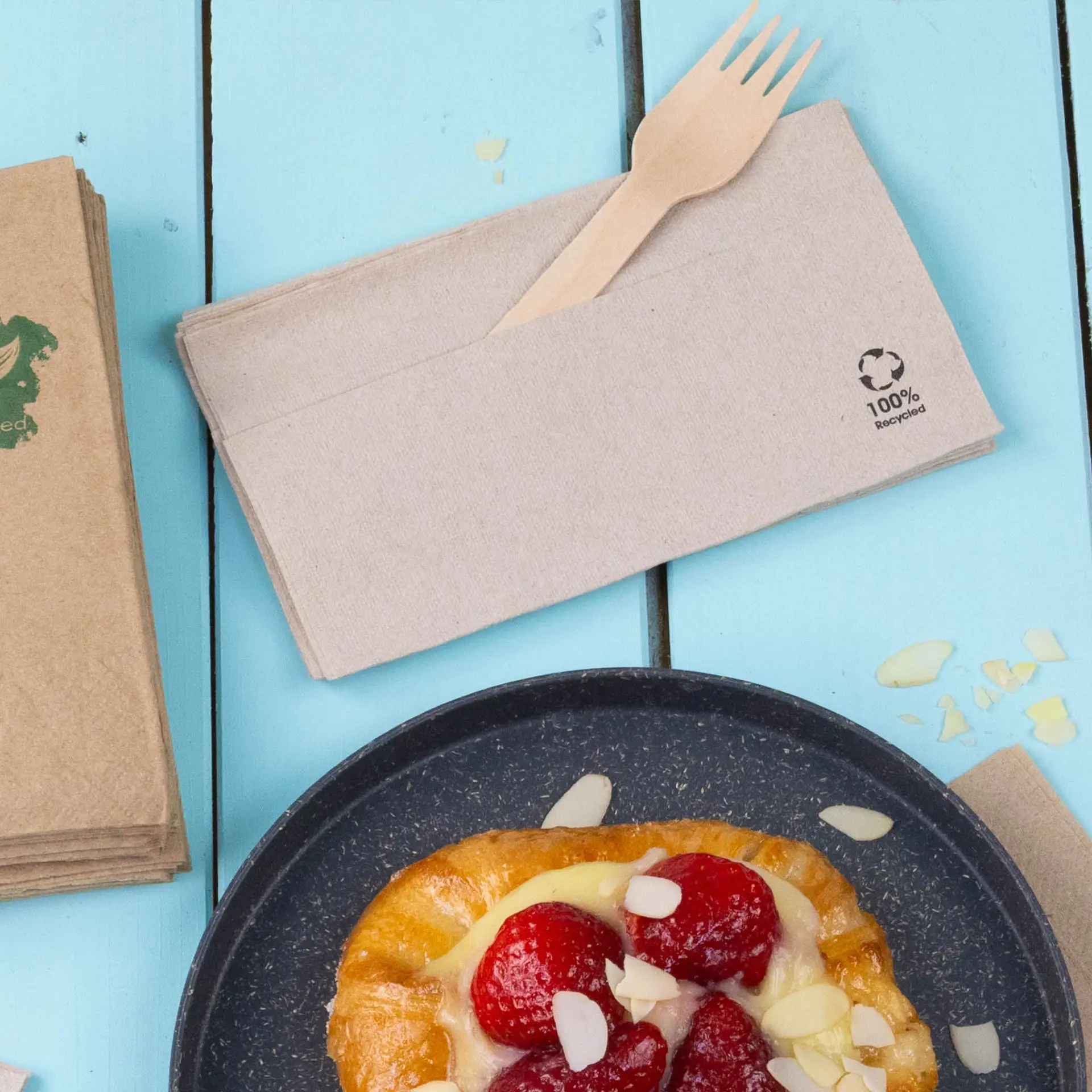 Paper napkins made of recycled paper, showing a wooden fork, on a light blue wooden surface.