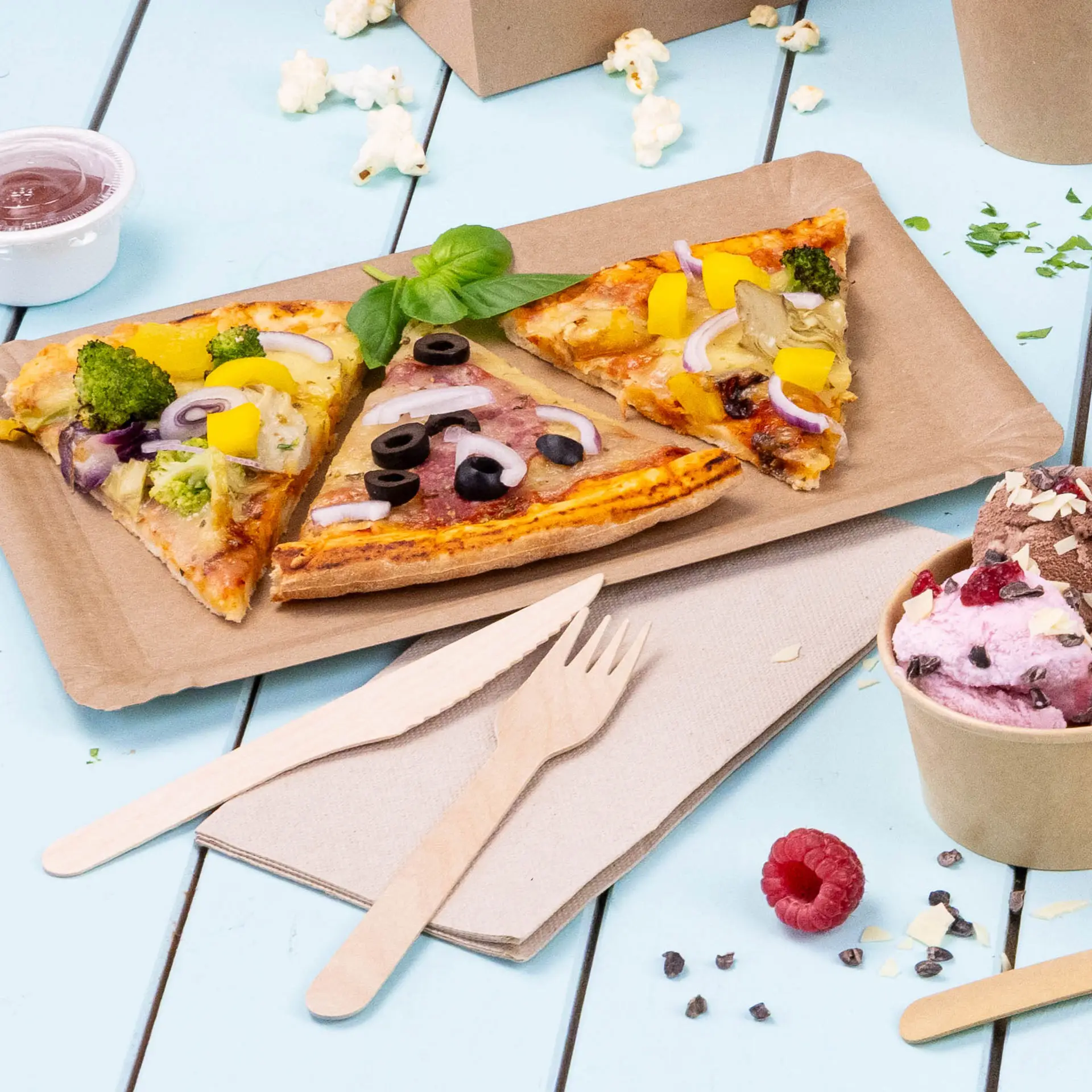 Bild von drei Pizzastücken mit verschiedenen Belägen auf einem braunen Pappteller, begleitet von Holzbesteck und einem Becher Eis.