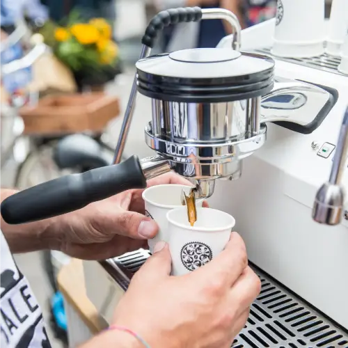 Two white disposable cups are positioned under an espresso machine dispensing coffee.