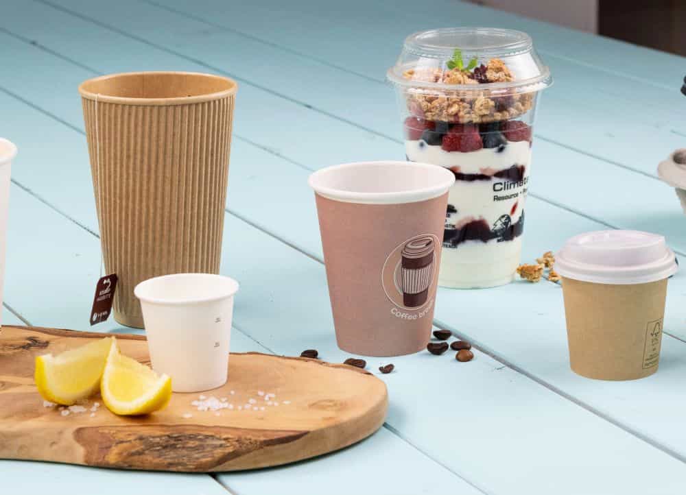 Multiple disposable cups and a dessert in a transparent cup, with lemon slices and salt on a wooden board.