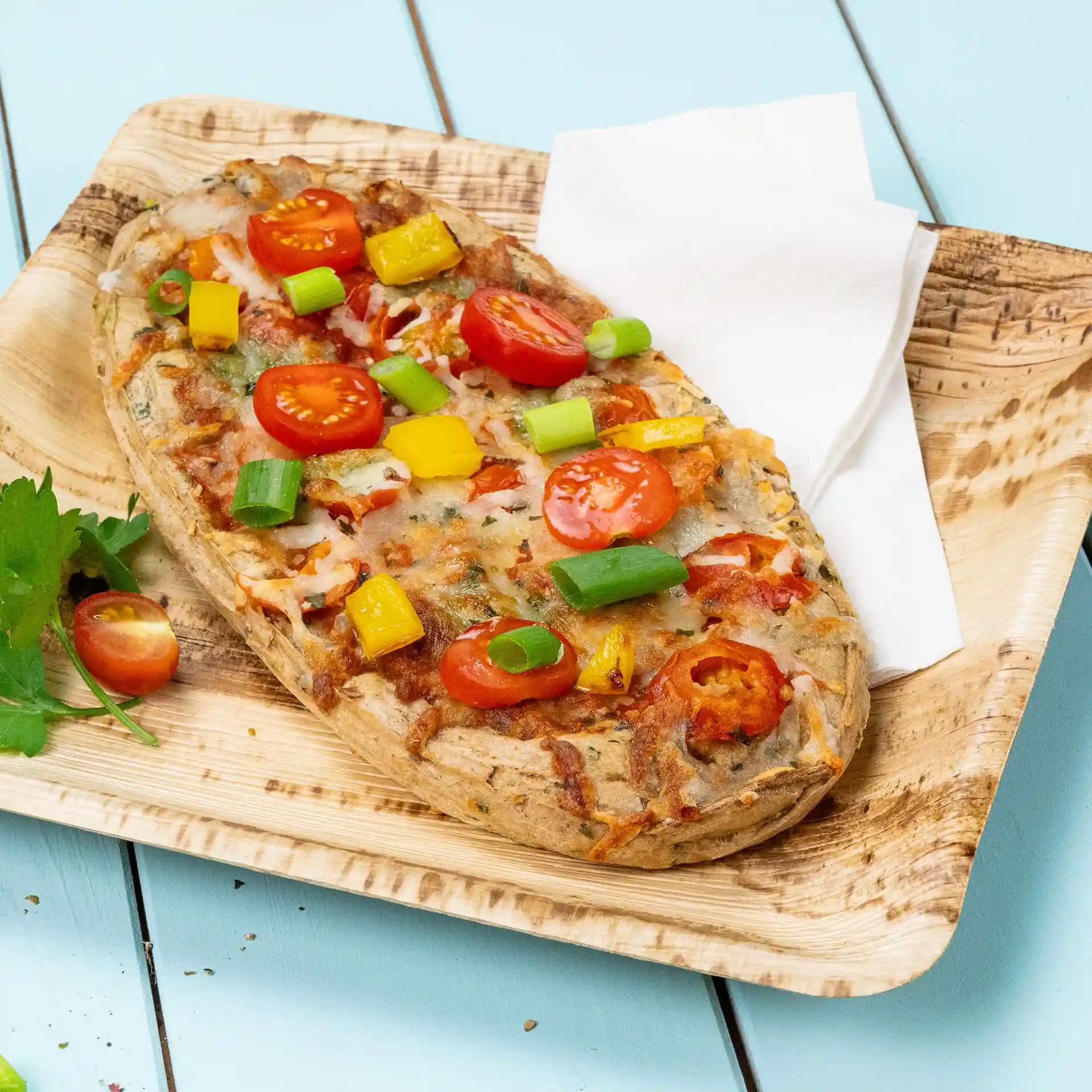 Fladenbrot belegt mit Kirschtomaten, gelben Paprika und Frühlingszwiebeln auf einem Holzbrett mit Serviette.
