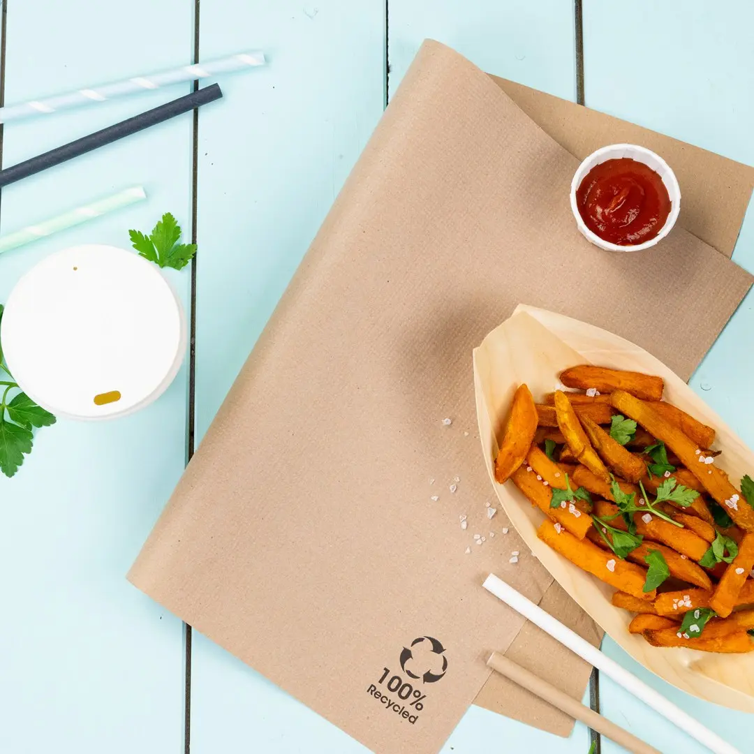 Brown kraft paper with sweet potato fries, ketchup, a white cup, and straws on a blue wooden surface.