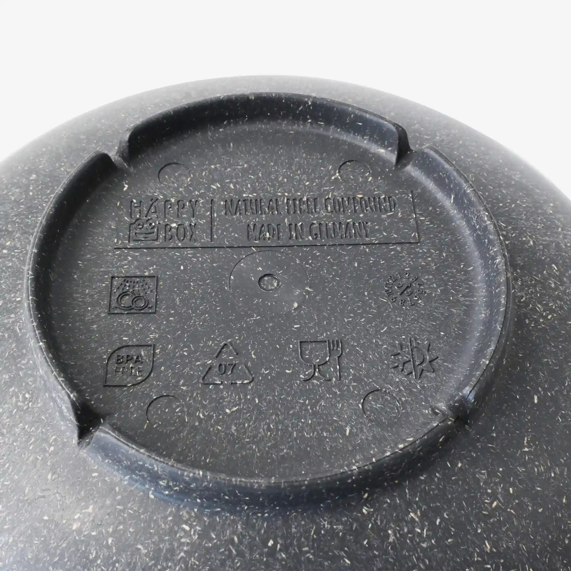 Bottom view of a round, deep grey plate made from bio compound, showing markings and symbols.