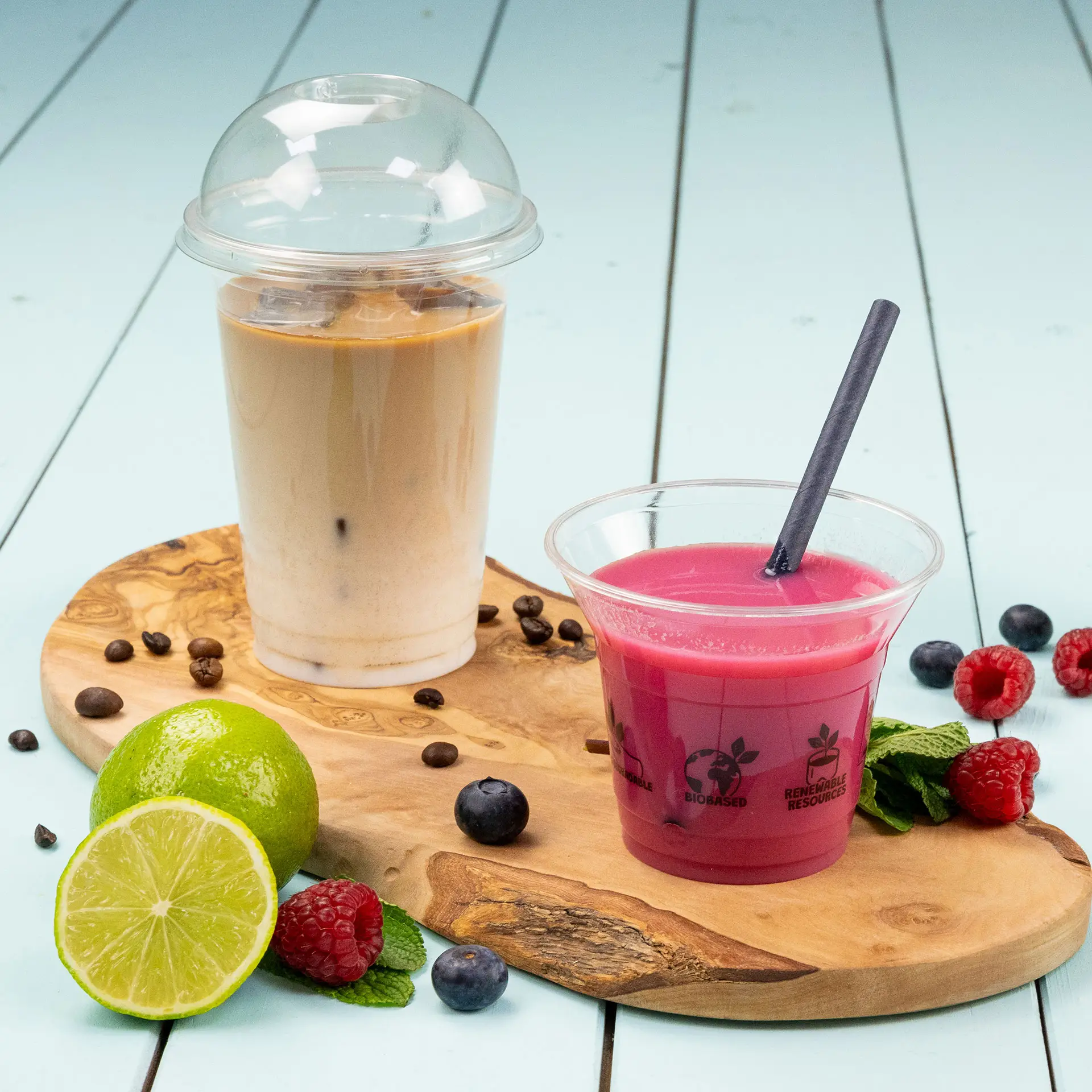 Transparente Becher mit kalten Getränken, darunter Eiskaffee und ein pinkes Getränk, auf einem Holzbrett.