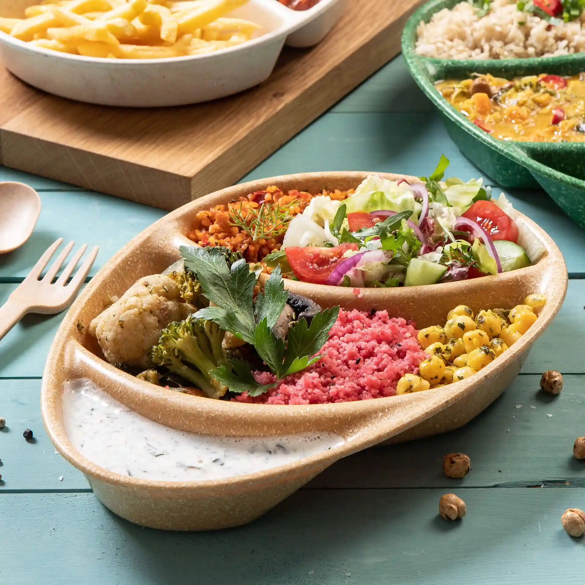 Reusable menu plate with three compartments, filled with various colorful foods and a sauce on a blue surface.