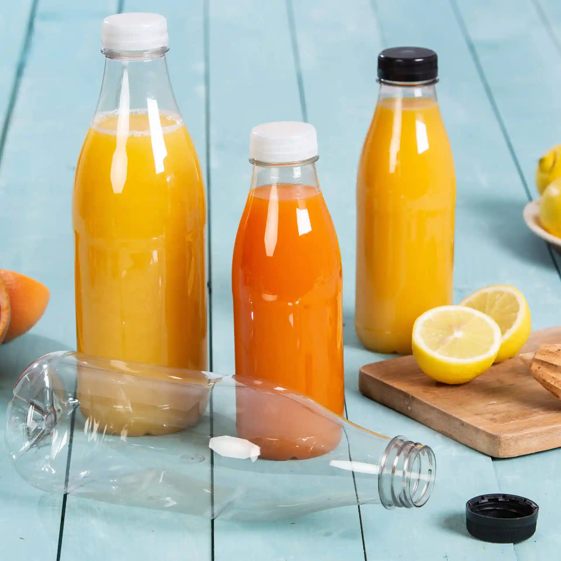 Bild von drei klaren rPET-Flaschen, gefüllt mit orangefarbenen und gelben Flüssigkeiten, eine Flasche ist umgekippt, mit Zitronenscheiben daneben.