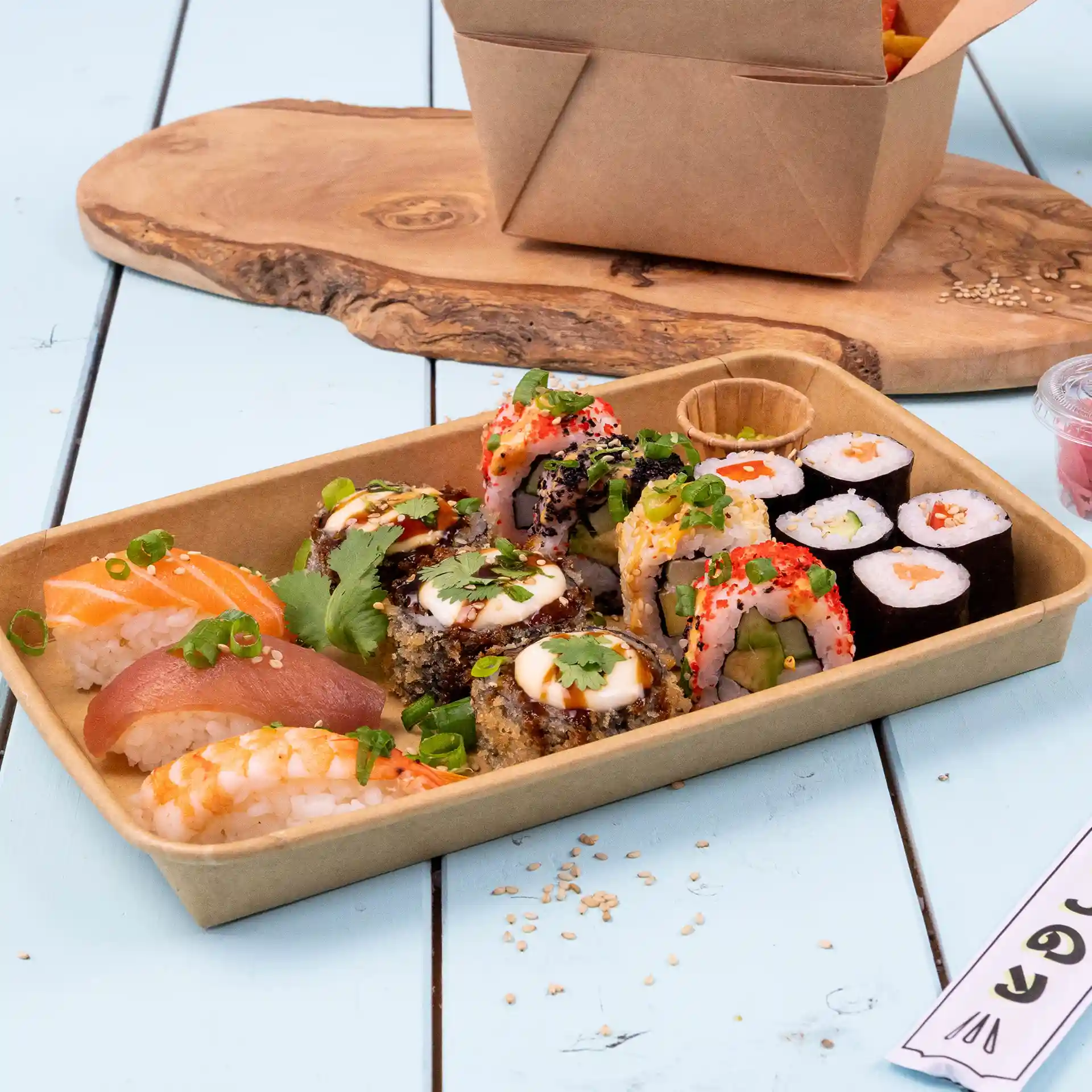Sushi-Auswahl in einer braunen PE-beschichteten Box, einschließlich verschiedener Rollen und Sashimi, auf einer Holzoberfläche.