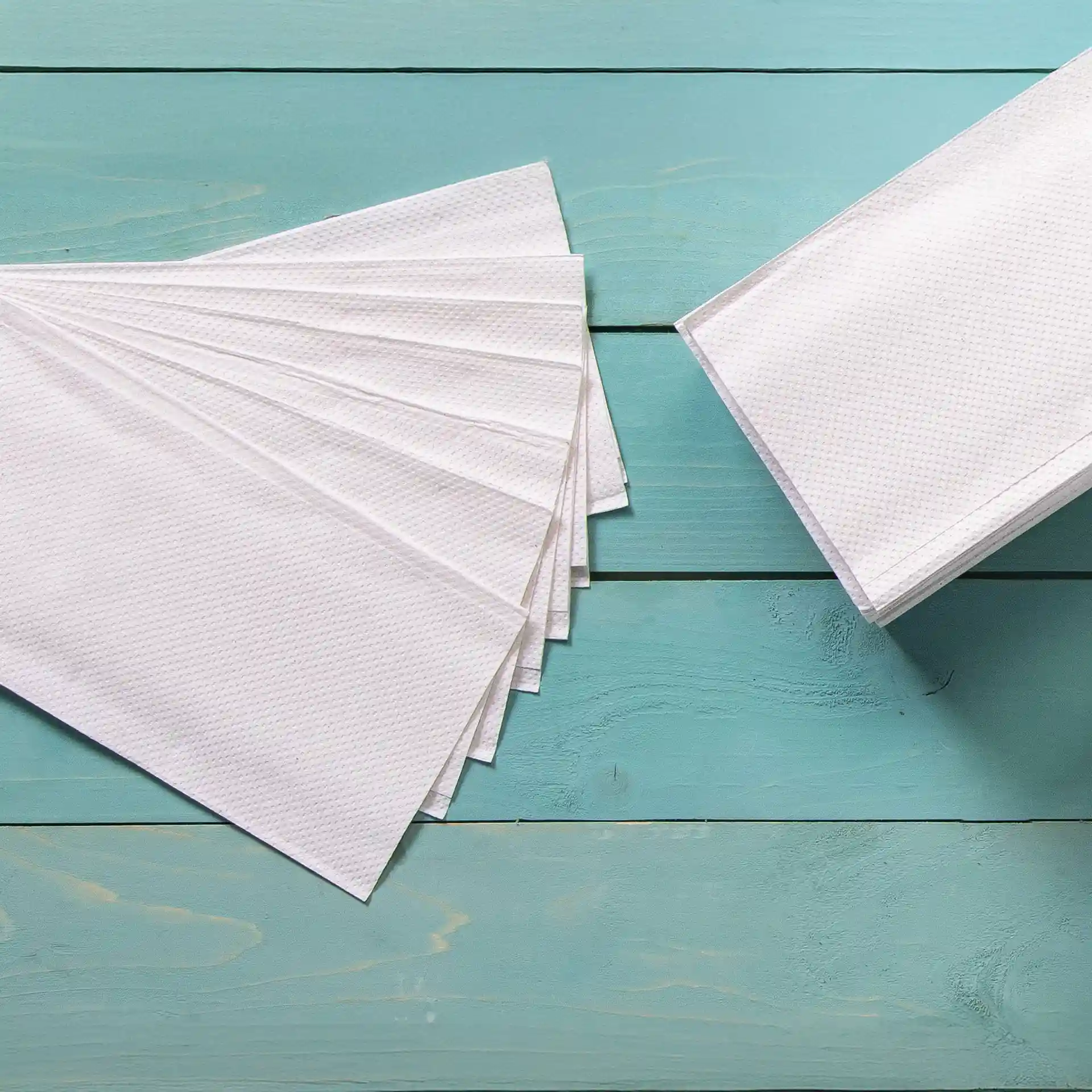 White 2-ply folded towels arranged in a fan shape next to a stack on a blue wooden surface.