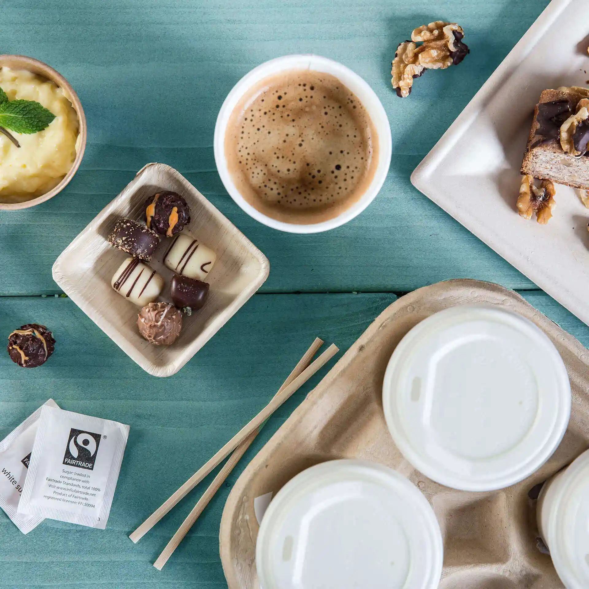 Image of a coffee cup, dessert, chocolates in a tray, and a paper bag on a blue wooden surface.