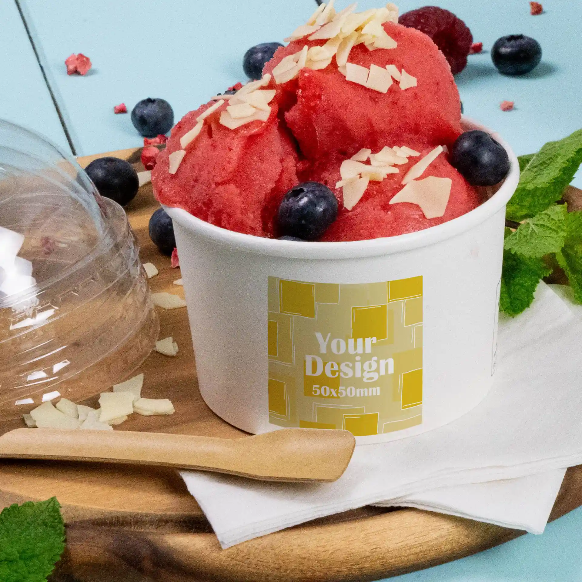 Becher mit rotem Sorbet, garniert mit Mandelblättchen und Heidelbeeren, in einem weißen matten Behälter mit Etikett.