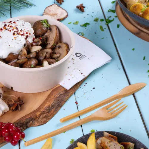 Schüssel mit sautierten Pilzen, garniert mit Joghurt und Gewürzen, dazu Holzutensilien auf blauem Hintergrund.