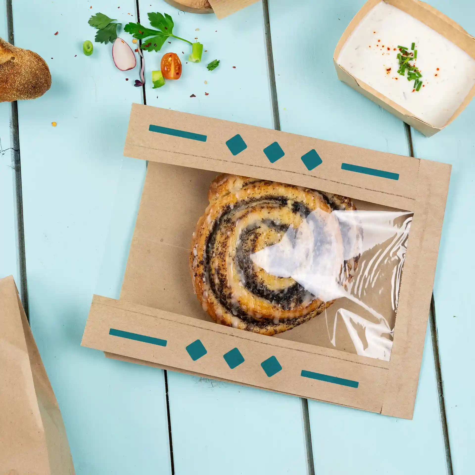 Brown printed paper bag with a transparent window, containing a spiral pastry, on a blue wooden surface.