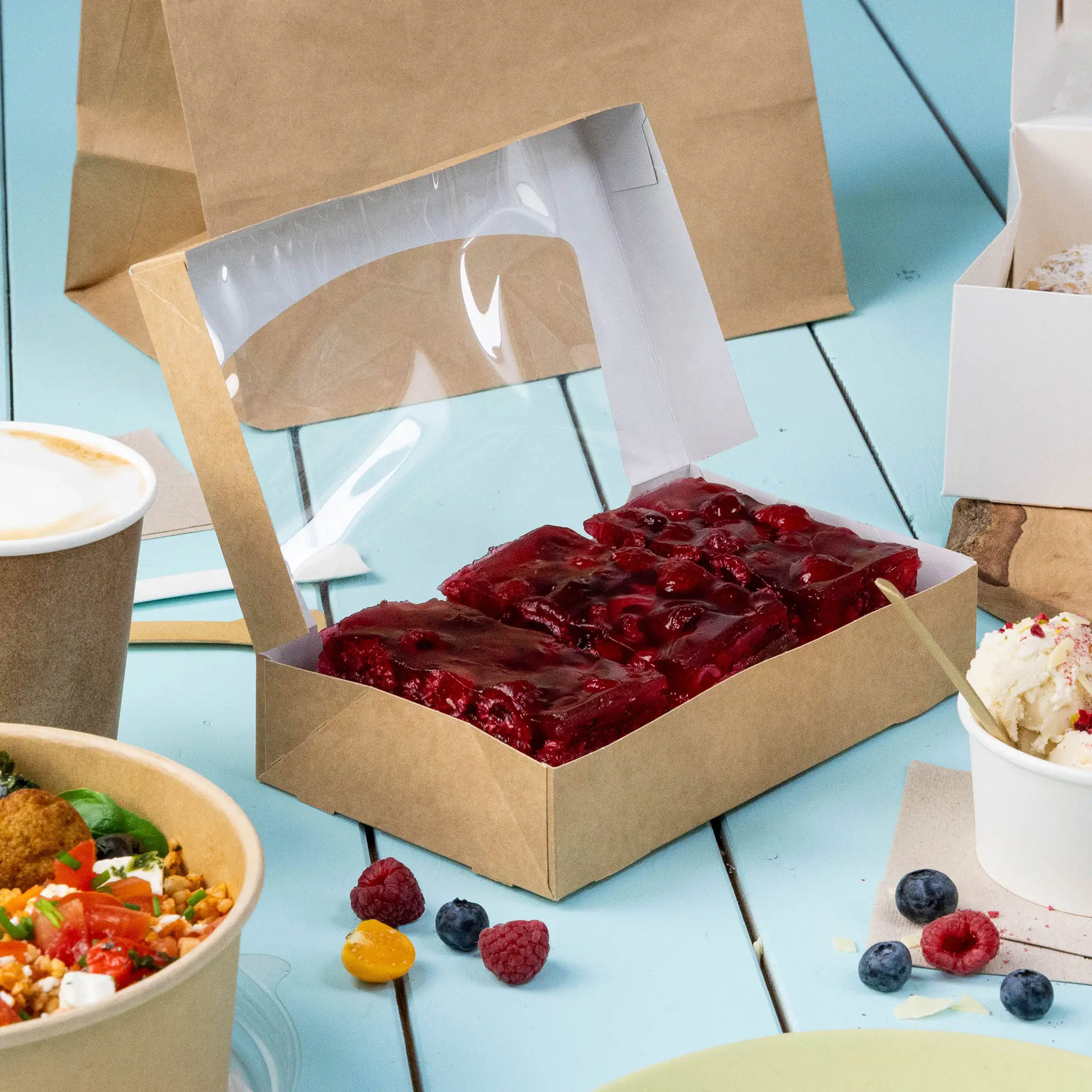 One windowed cardboard folding box with a clear cellulose top, containing red pastries, on a blue background with additional food items.