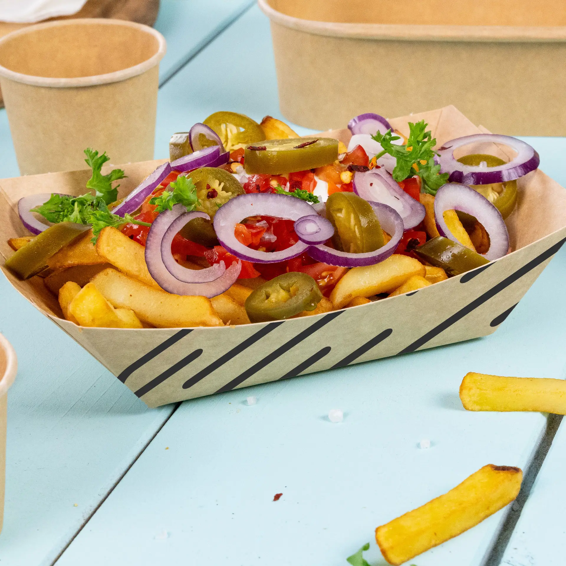 Custom-printed brown snack tray filled with fries, jalapeños, onion slices, and fresh toppings, on a blue surface.