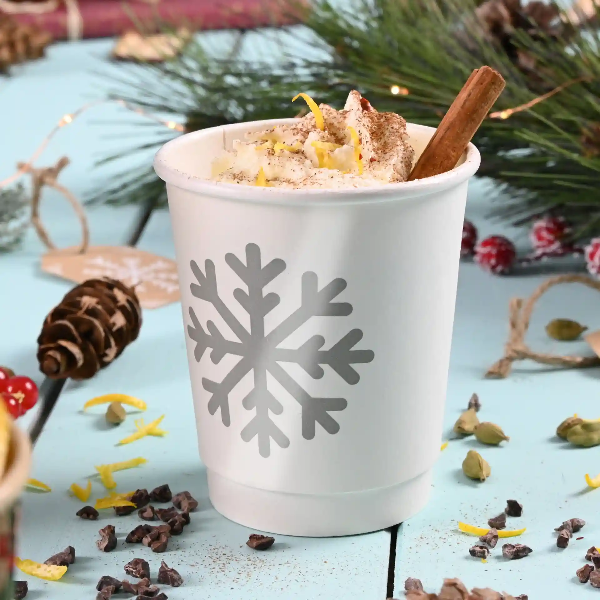 White double-walled paper cup with a gray snowflake design, filled with whipped cream and a cinnamon stick.