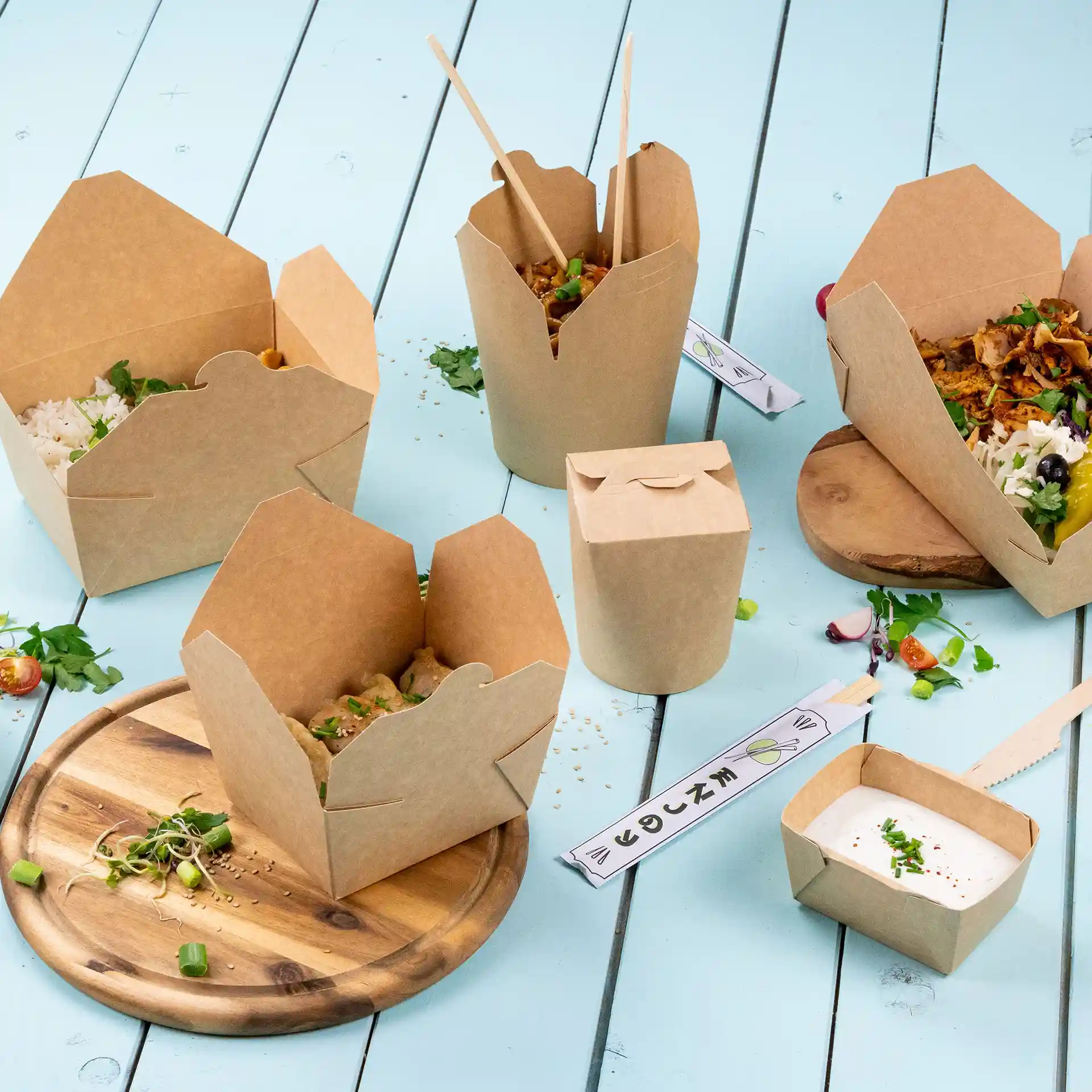 Image of multiple brown cardboard take-away boxes with food, placed on a light blue surface and a wooden board.