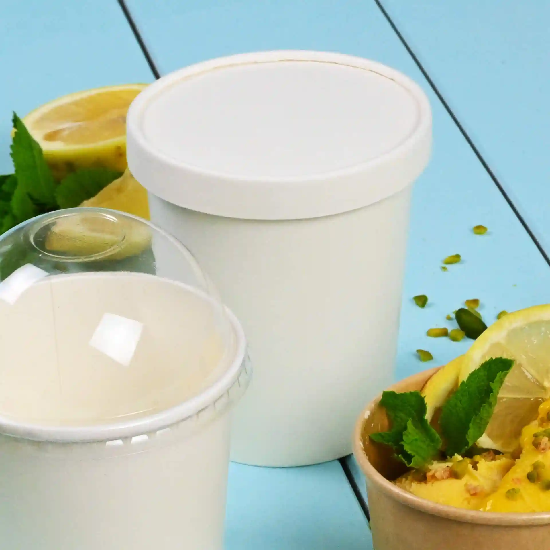 Weißer runder Papierdeckel für Eisbecher, neben einem weißen Becher mit Zitronenscheiben und Minzblättern.