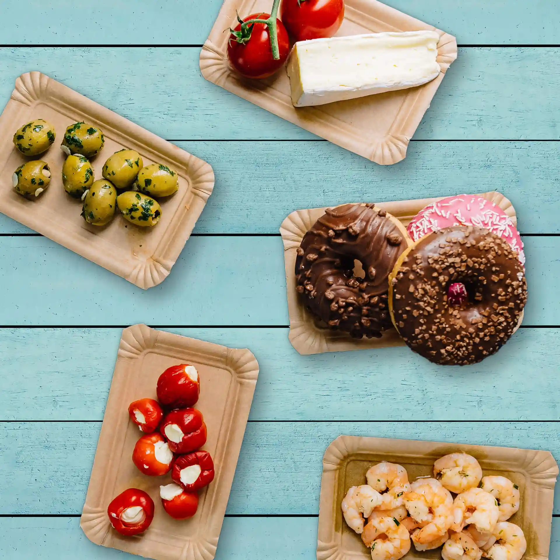 Bild von mehreren rechteckigen braunen Papptellern mit verschiedenen Lebensmitteln: Oliven, Tomaten, Käse, Donuts und Garnelen.
