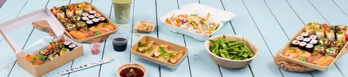 Eine Auswahl an Sushi-Rollen wird präsentiert, einschließlich einer Sushi-Box, Sojasauce und Wasabi auf einer Bambusmatte.