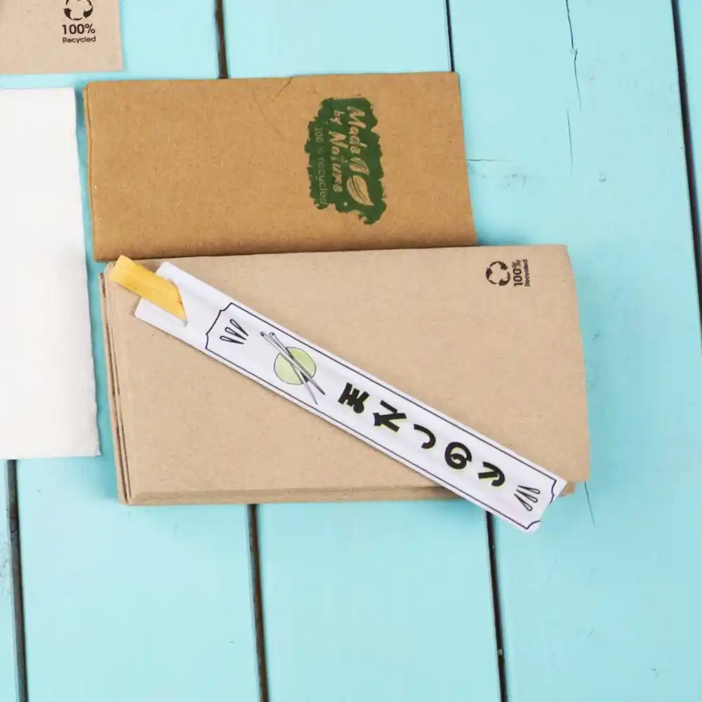 Essstäbchen in Papier gewickelt auf einer blauen Holzoberfläche, mit einer braunen Kraftpapierbox im Hintergrund.