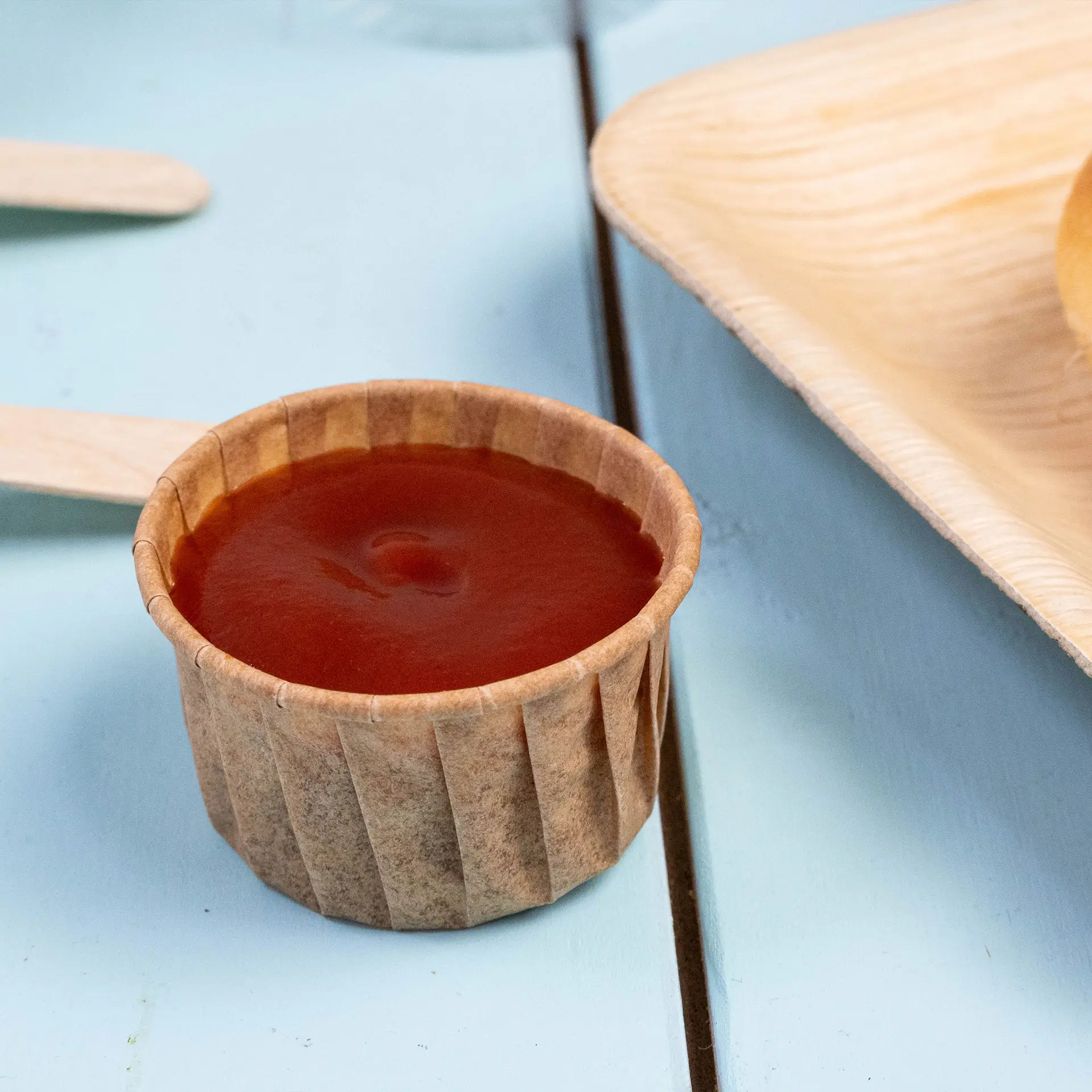 Brown paper dip cup filled with ketchup on a blue surface, designed for sauces and small portion servings.
