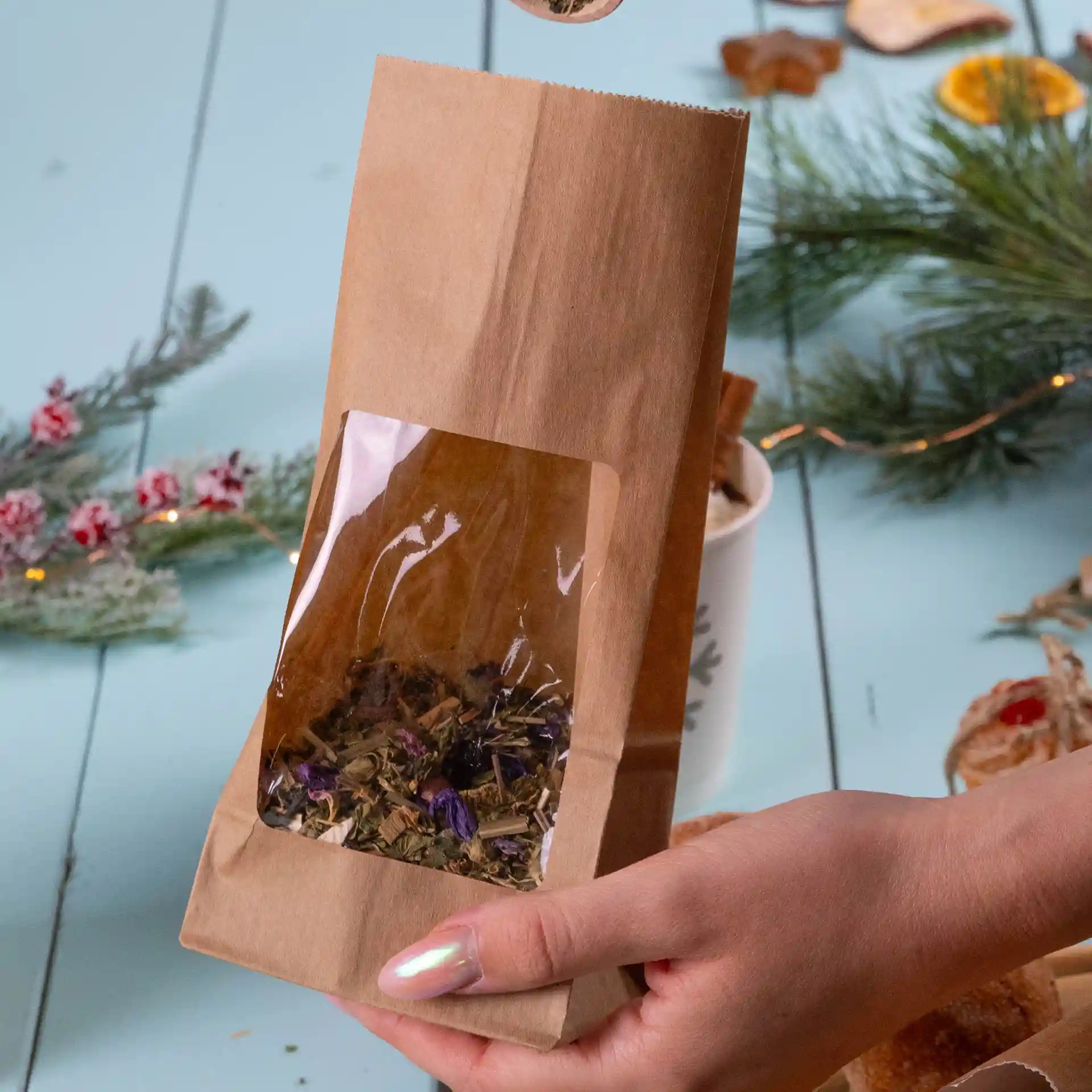 Brown kraft paper bag with a transparent window, containing dried herbs, held by a hand.