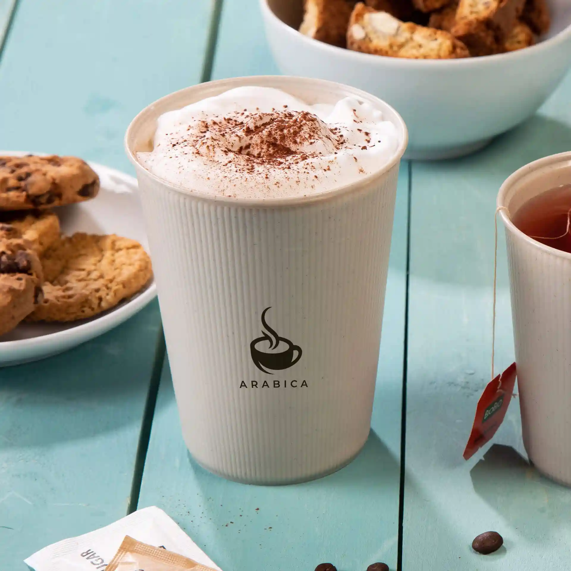 Reusable cup with a ripple design, filled with whipped cream and cocoa powder, beside cookies and tea.
