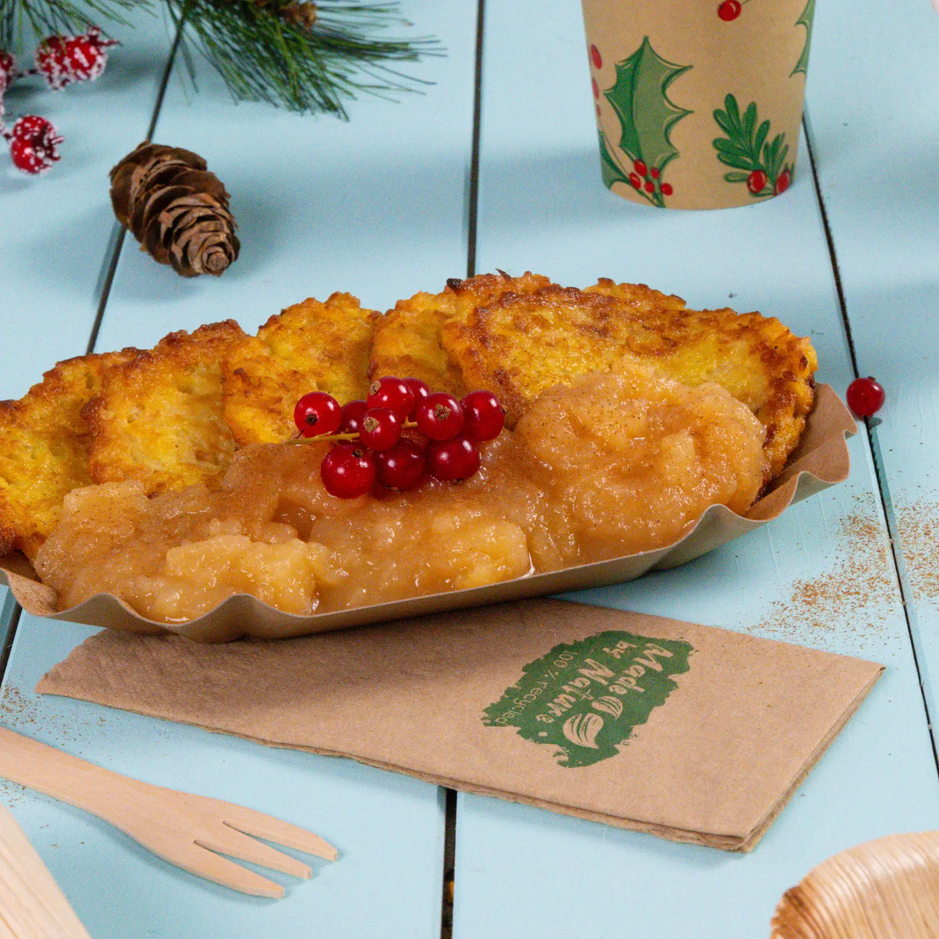 Ein Teller mit frittierten Speisen und Apfelmus, garniert mit roten Beeren; umgeben von festlicher Dekoration und Servietten.