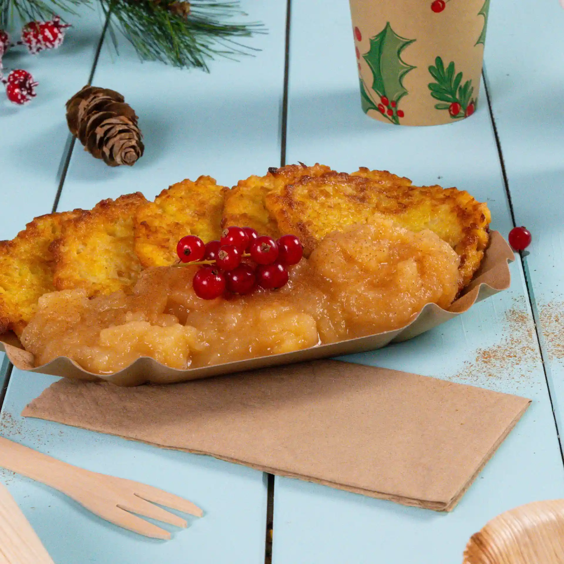 Teller mit mehreren goldbraunen Puffern, Apfelmus und roten Johannisbeeren auf einer hellblauen Holzoberfläche mit Serviette.