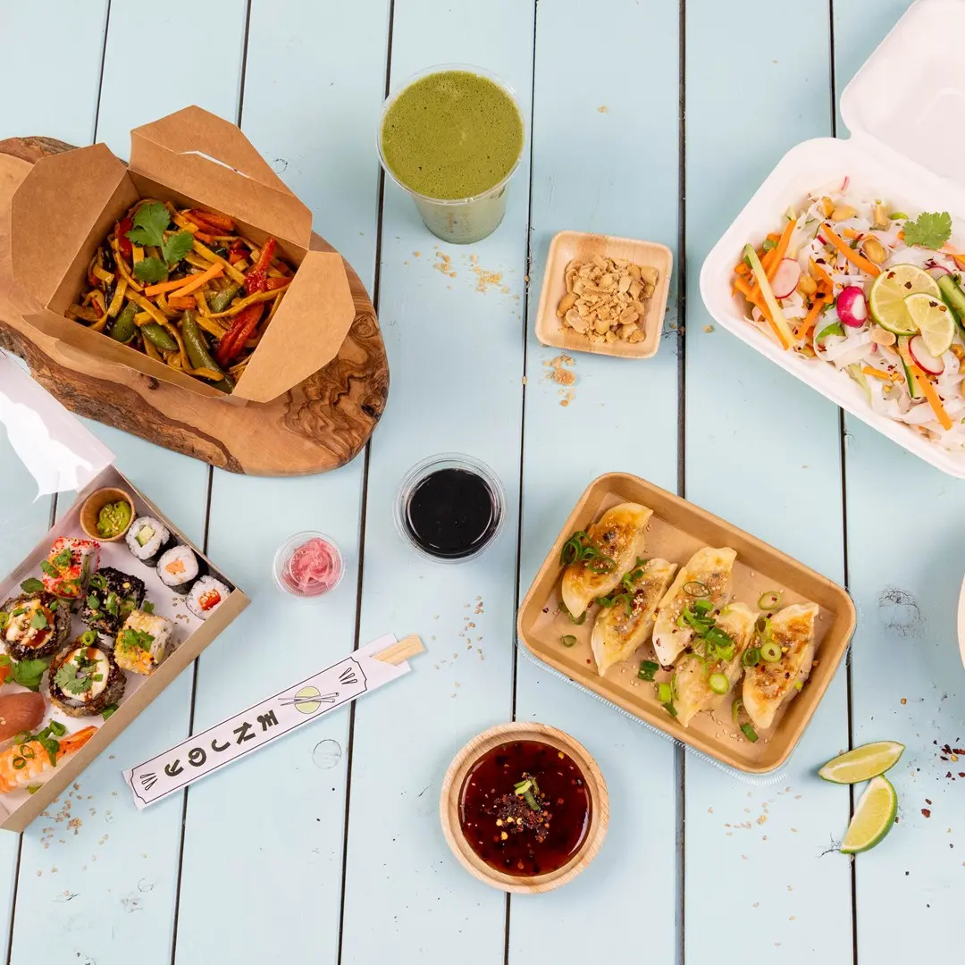 Assorted Asian dishes including sushi, dumplings, stir-fried vegetables, and a green drink on a blue wooden table.