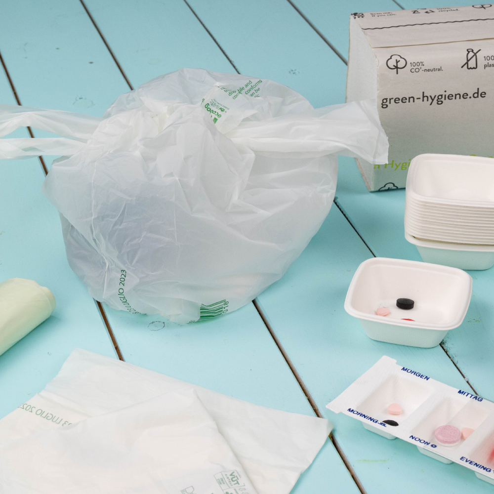 Plastic bag containing hygiene products; a white bowl with assorted items and a box labeled "green-hygiene.de" nearby.