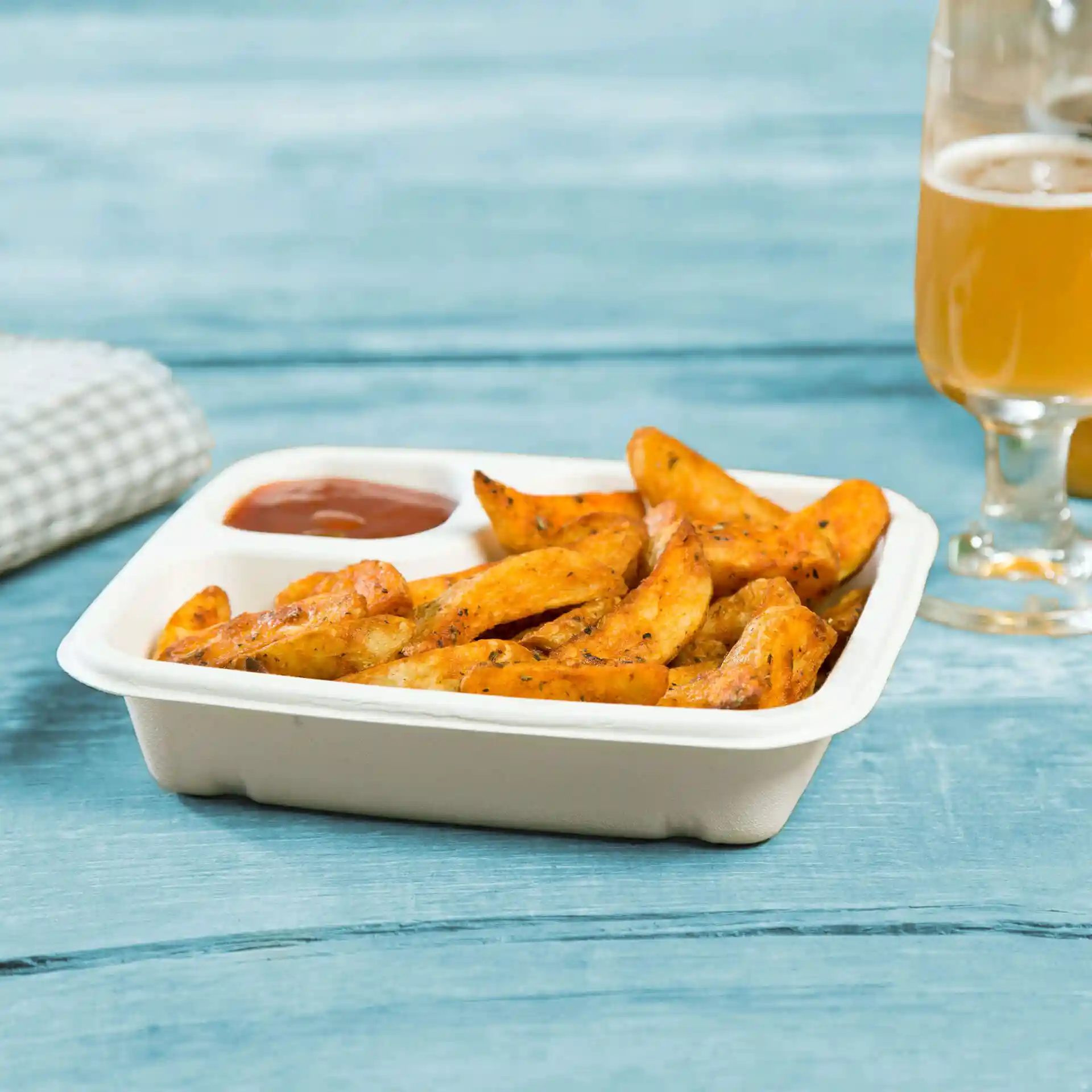 Rectangular white sugarcane dip plate with potato wedges and a portion of sauce on a blue wooden surface.