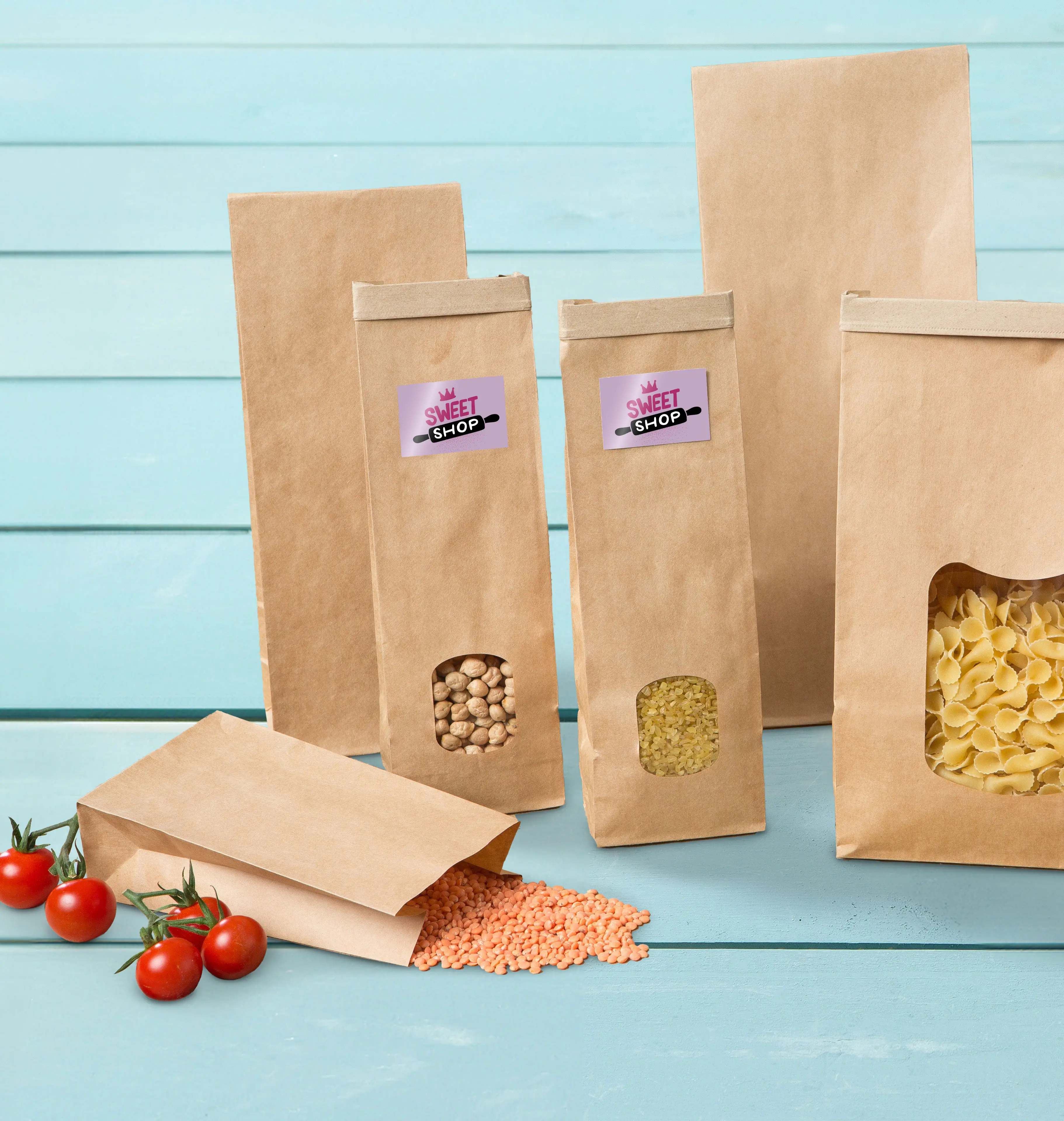 Brown paper bags in various sizes with see-through windows, filled with lentils, chickpeas, and pasta, on a blue wood surface.
