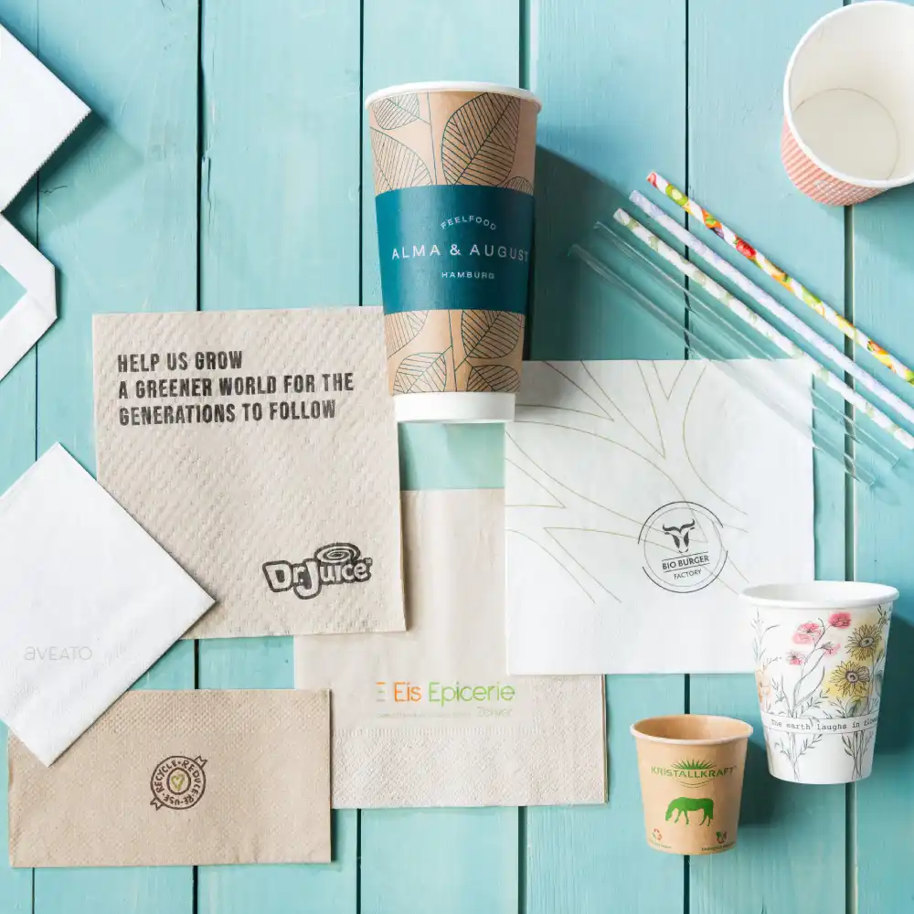 Eine Vielzahl bedruckter Verpackungsmaterialien, darunter Becher, Servietten und Strohhalme auf einer Holzoberfläche.