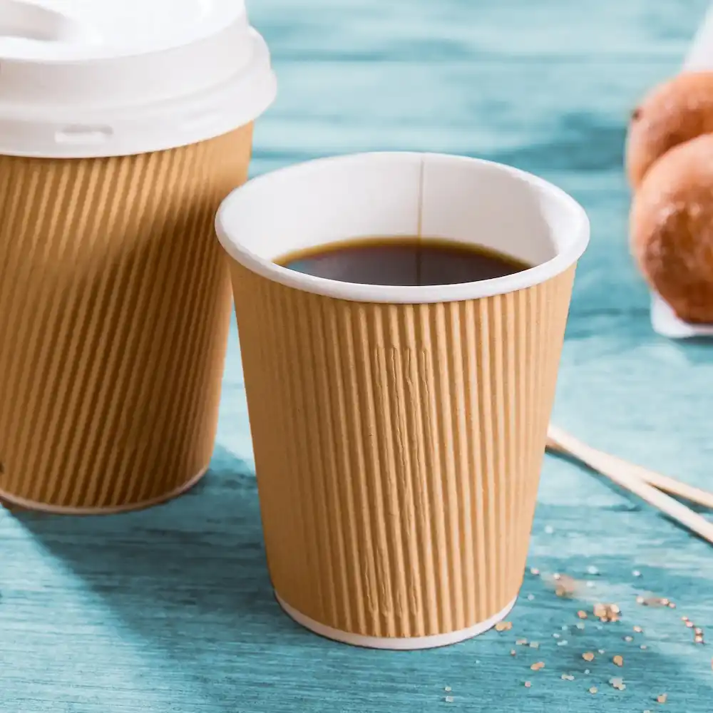 Brown ribbed paper coffee cup with black coffee, next to a similar cup and doughnuts on a blue surface.