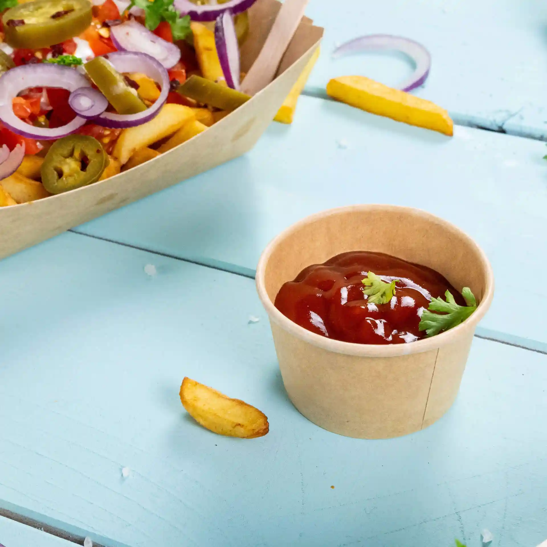 Brown paper portion cup with ketchup and a garnish of cilantro, placed on a light blue surface.