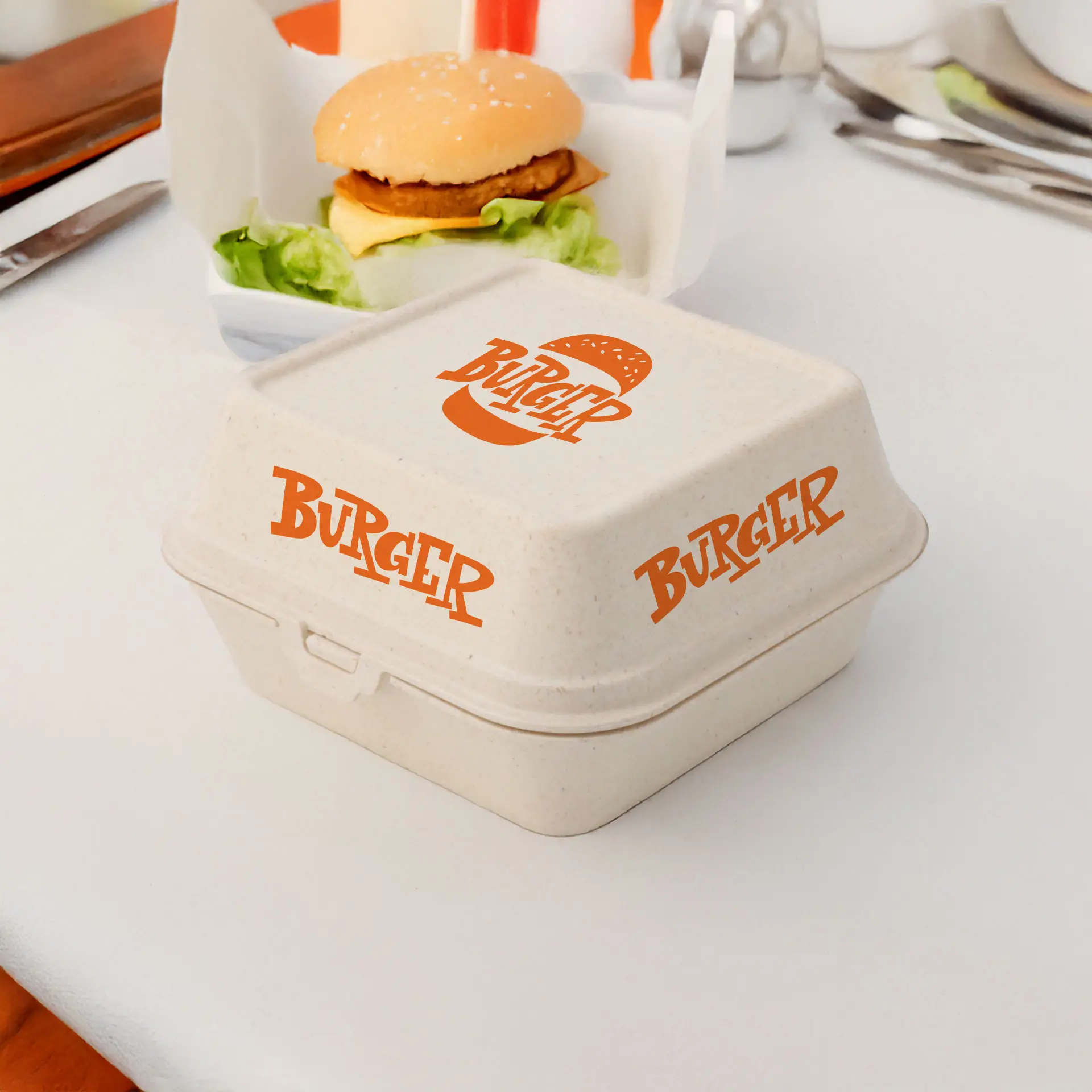 Cremeweiße wiederverwendbare Burgerbox mit orangefarbenem "BURGER"-Logo, geeignet für heiße und kalte Speisen, neben einem Hamburger auf einem Tisch.