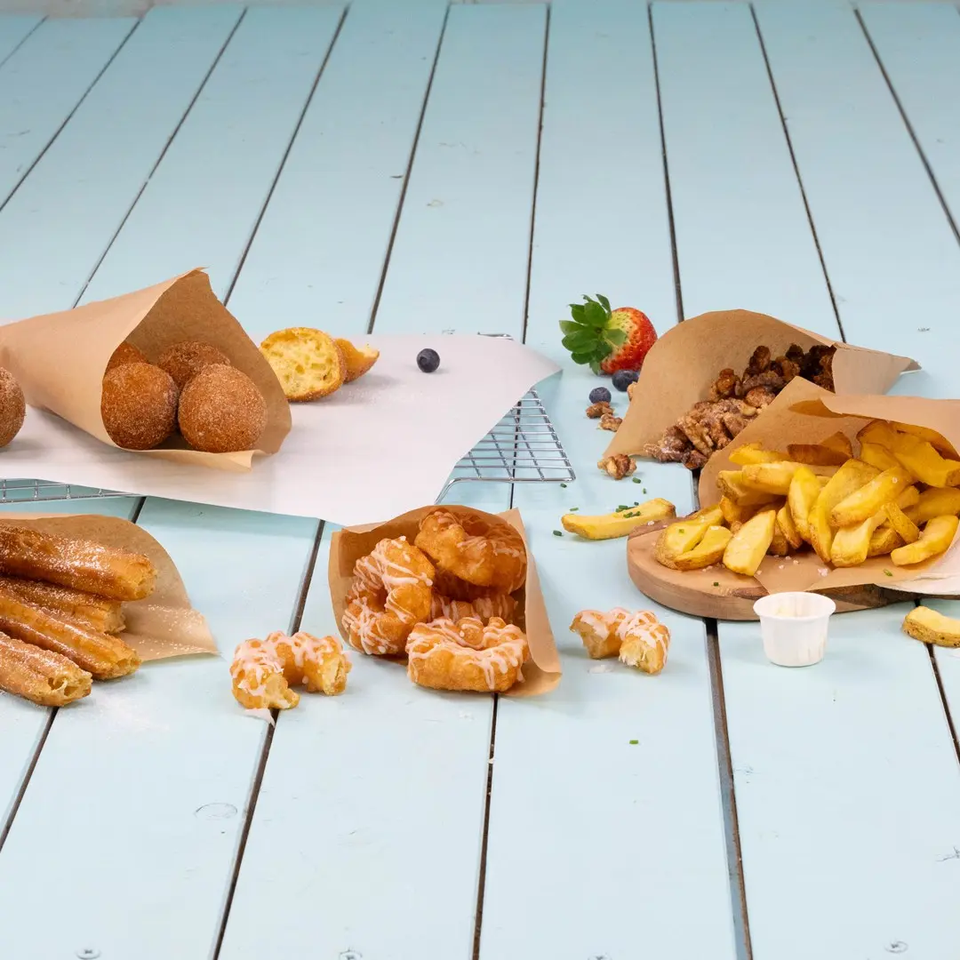 Assorted fried foods and pastries served in paper wrappers on a light blue wooden surface.