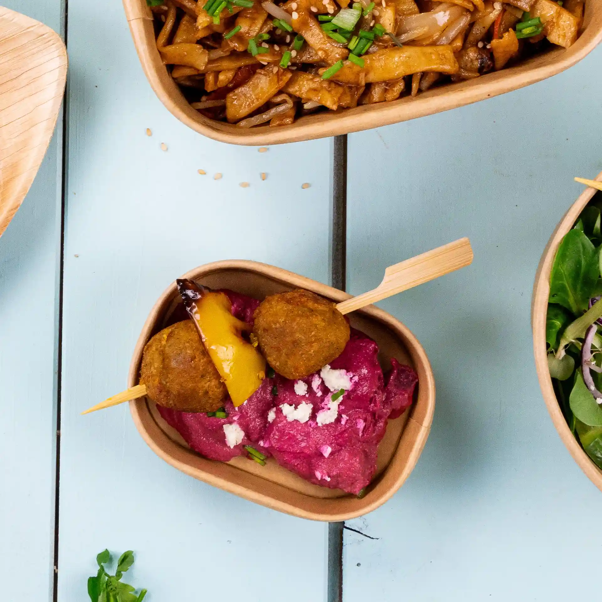 Bamboo paddle skewers with two golden-brown balls and a piece of yellow pepper on a bed of pink dip in a brown bowl.