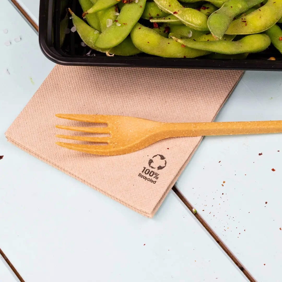 Brown napkin with a yellow fork placed on it, next to a black container of edamame beans.