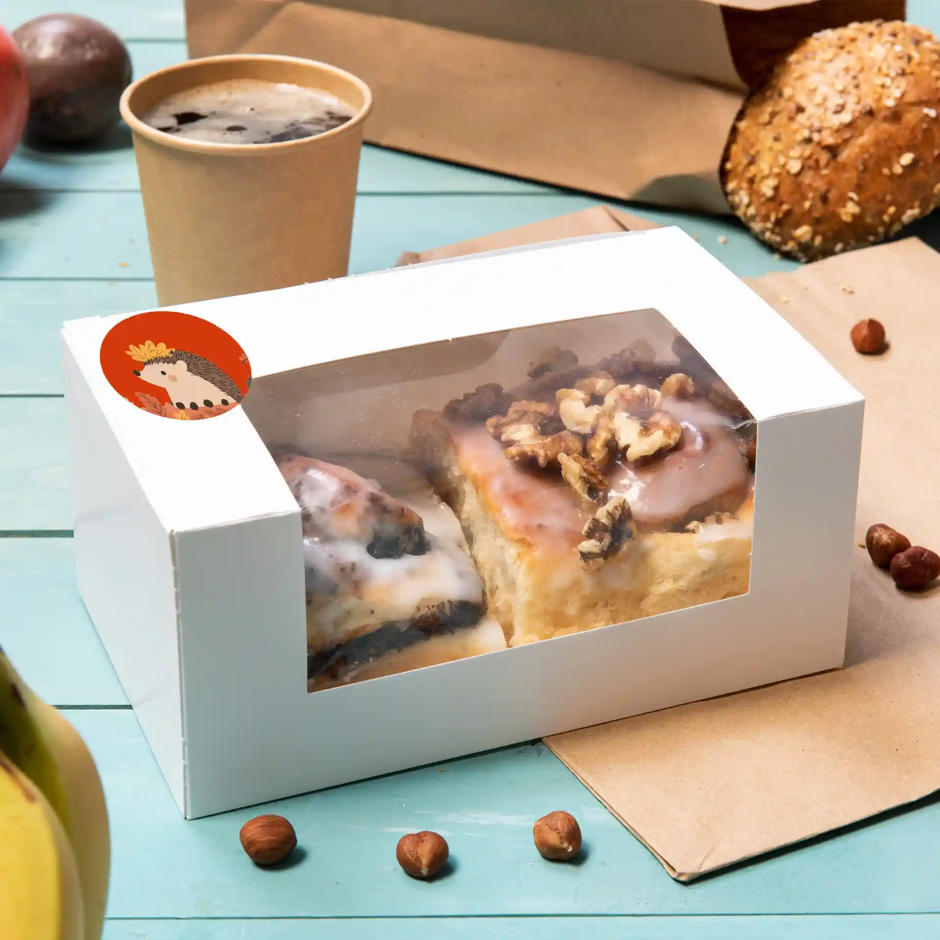 White box with a clear window containing two pastries topped with icing and walnuts, with a printed label on the side.