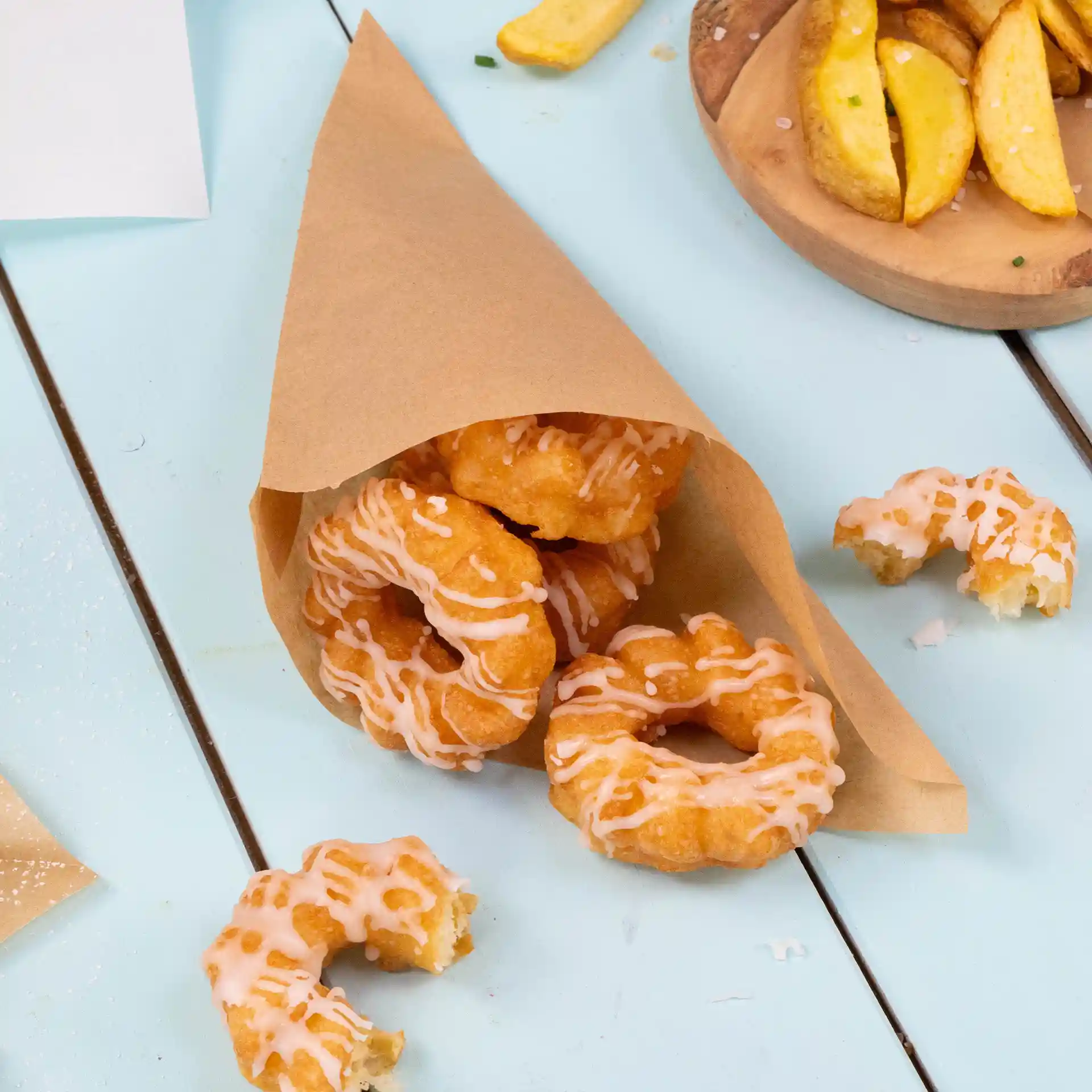 Brown paper bag containing several fried donuts with icing, placed on a light blue surface.