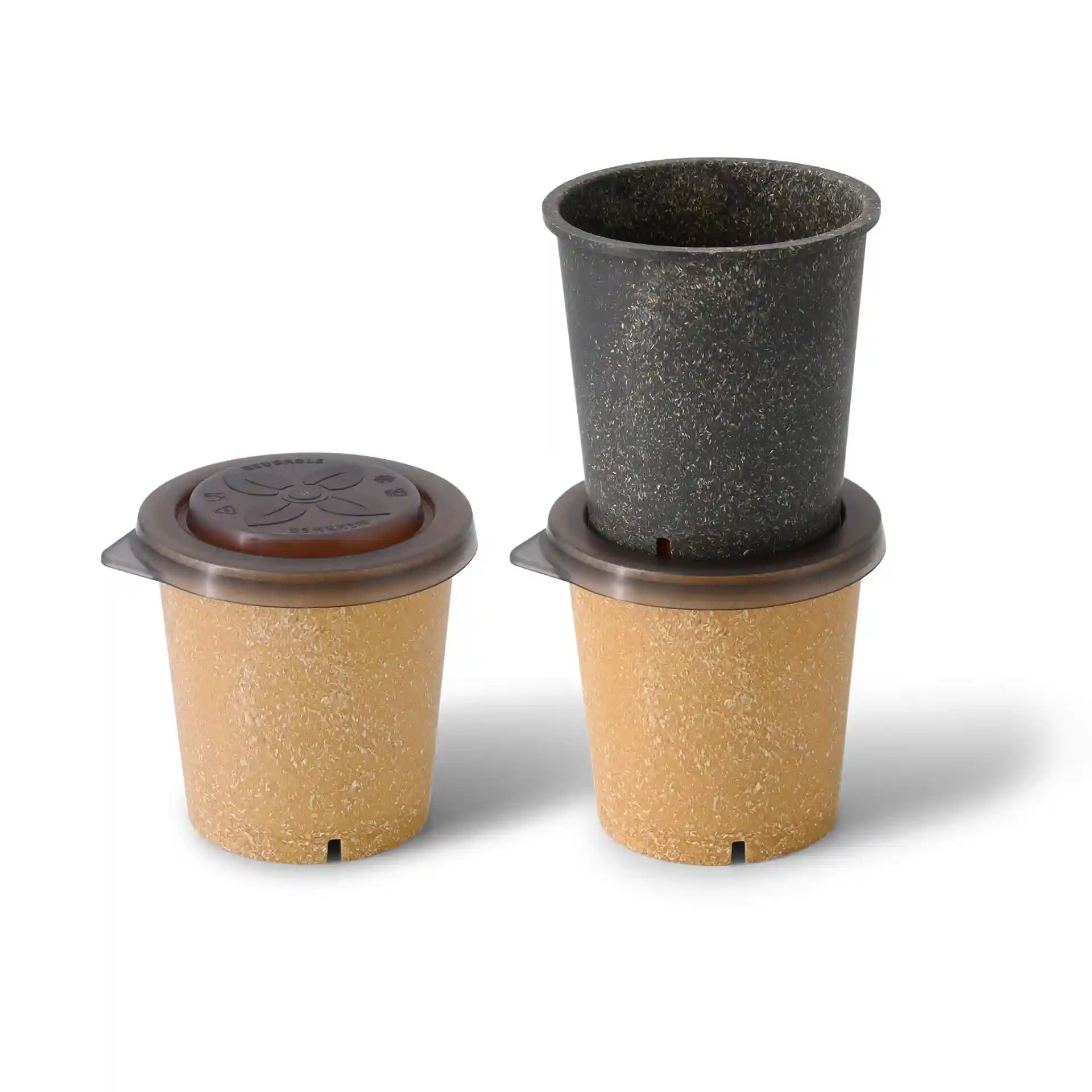 Drei wiederverwendbare Becher in Beige und Schwarz, mit einem braunen Deckel auf dem obersten Becher, auf einem schlichten Hintergrund angeordnet.
