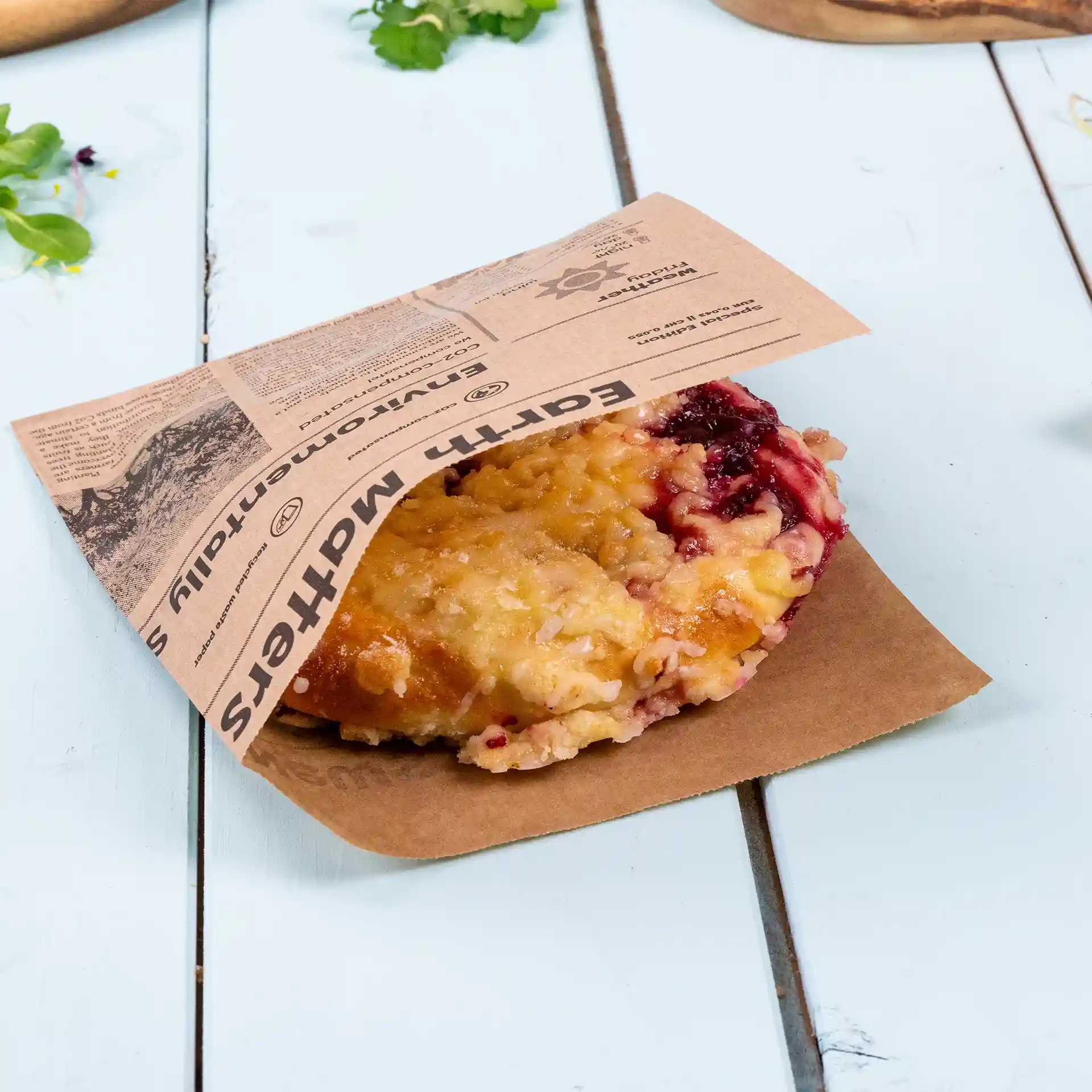 Papier-Burgerbeutel im Zeitungslook, enthält ein gebackenes Produkt, auf einer hellblauen Oberfläche platziert.