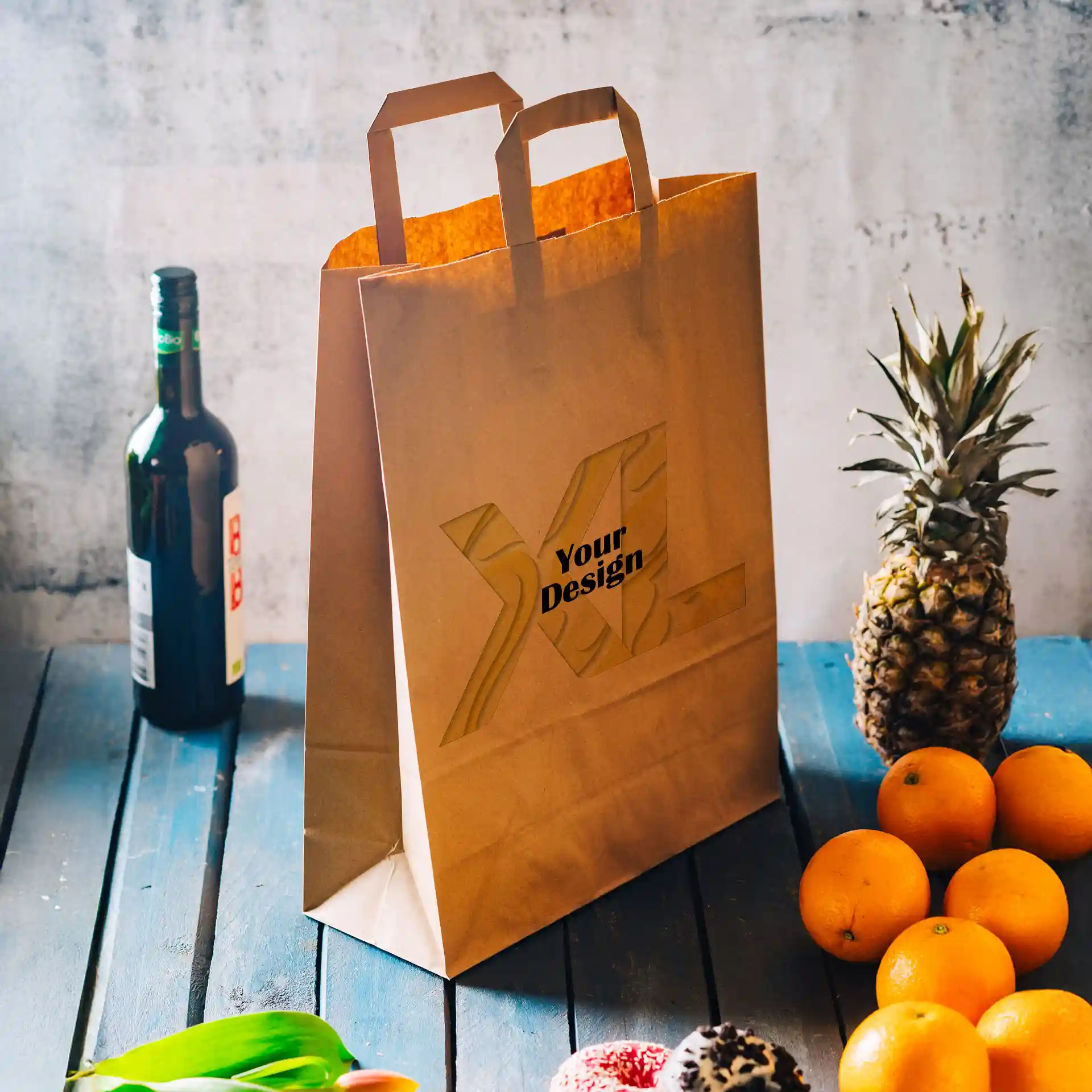 Braune Papiertasche mit zwei Griffen, mit einem Designbereich, neben Früchten und einer Flasche auf einer blauen Holzoberfläche.