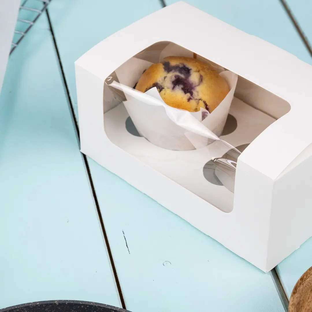 White cupcake box with a clear window displaying a blueberry muffin inside.
