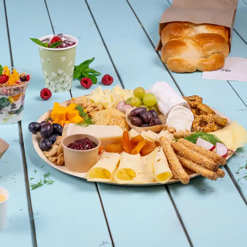 Platte mit verschiedenen Käsesorten, Crackern, Früchten, Nüssen und Brot auf einer blauen Holzoberfläche.