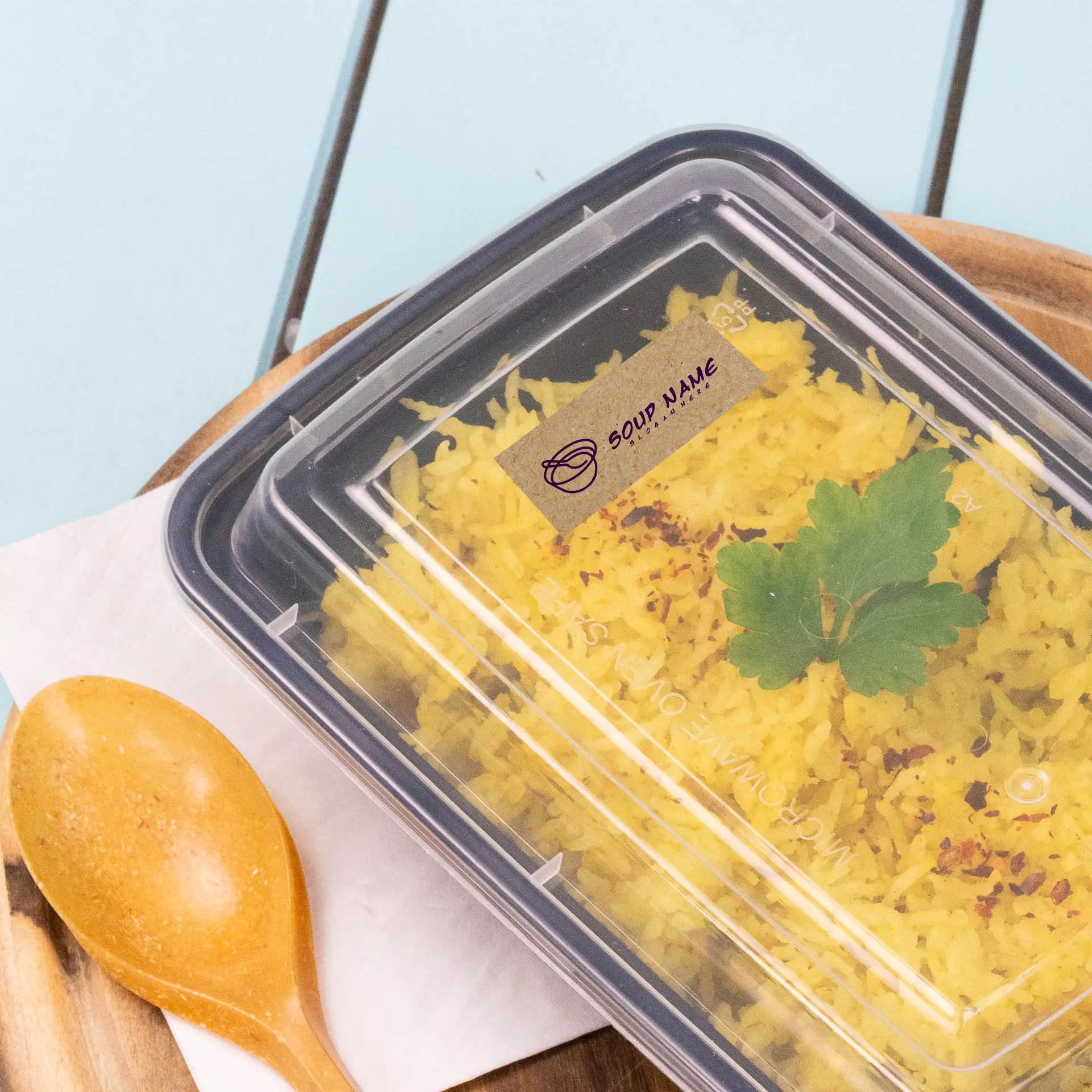 Container with yellow rice topped with cilantro and a printed label, accompanied by a wooden spoon on a wooden surface.